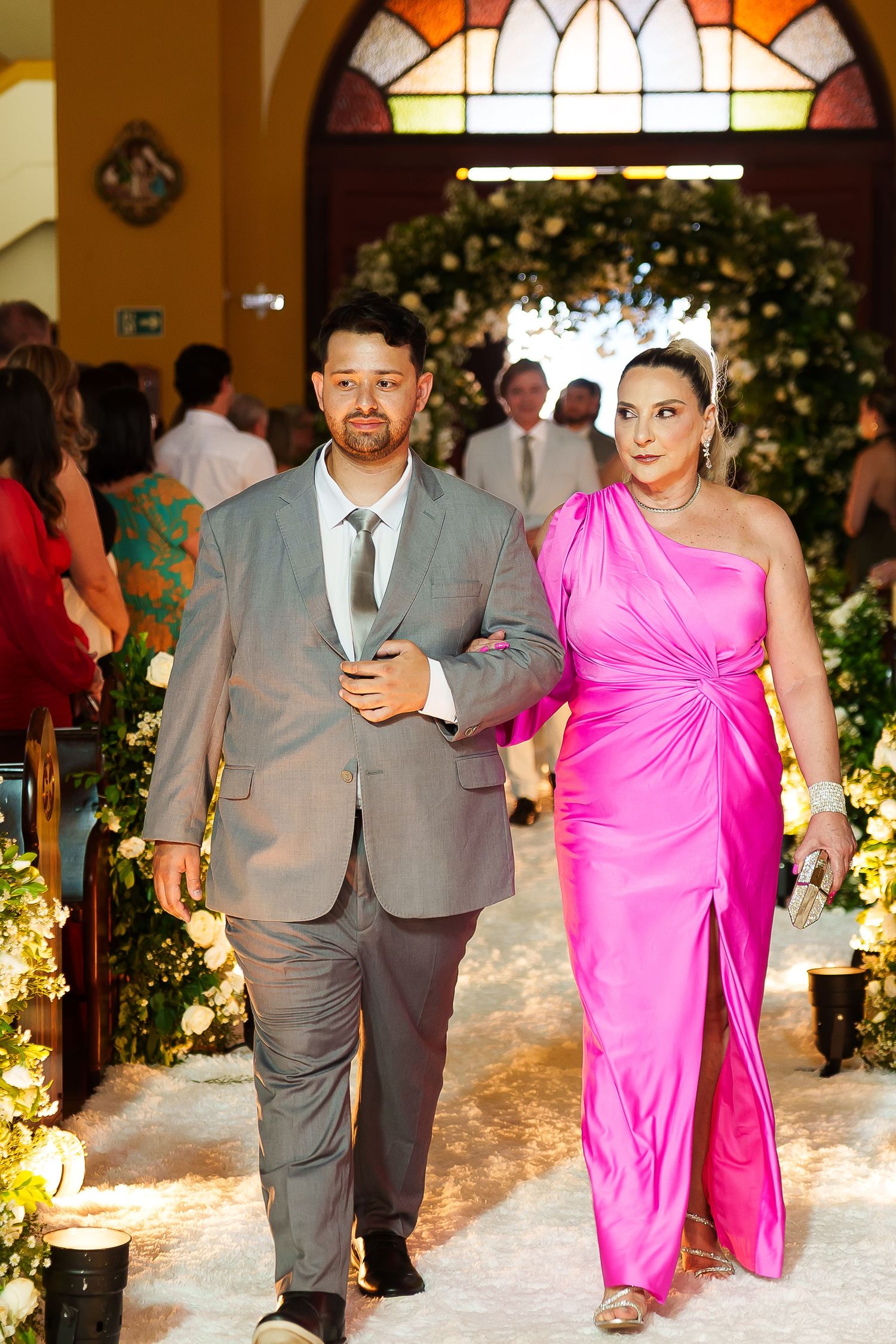 Couple walking down wedding aisle, man in gray suit, woman in pink gown, church ceremony.