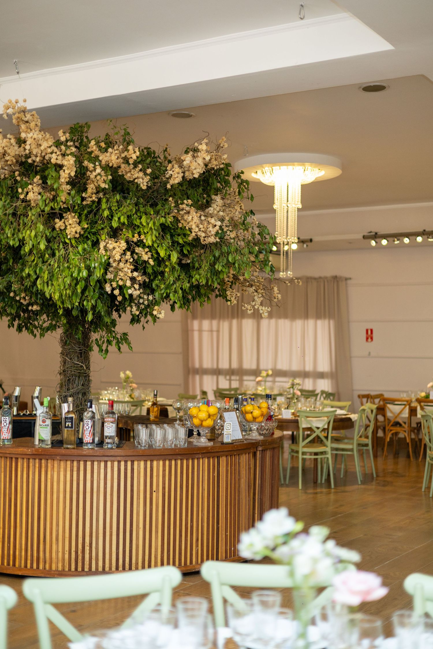 Elegant wedding reception venue with a large floral tree centerpiece over a wooden circular bar.