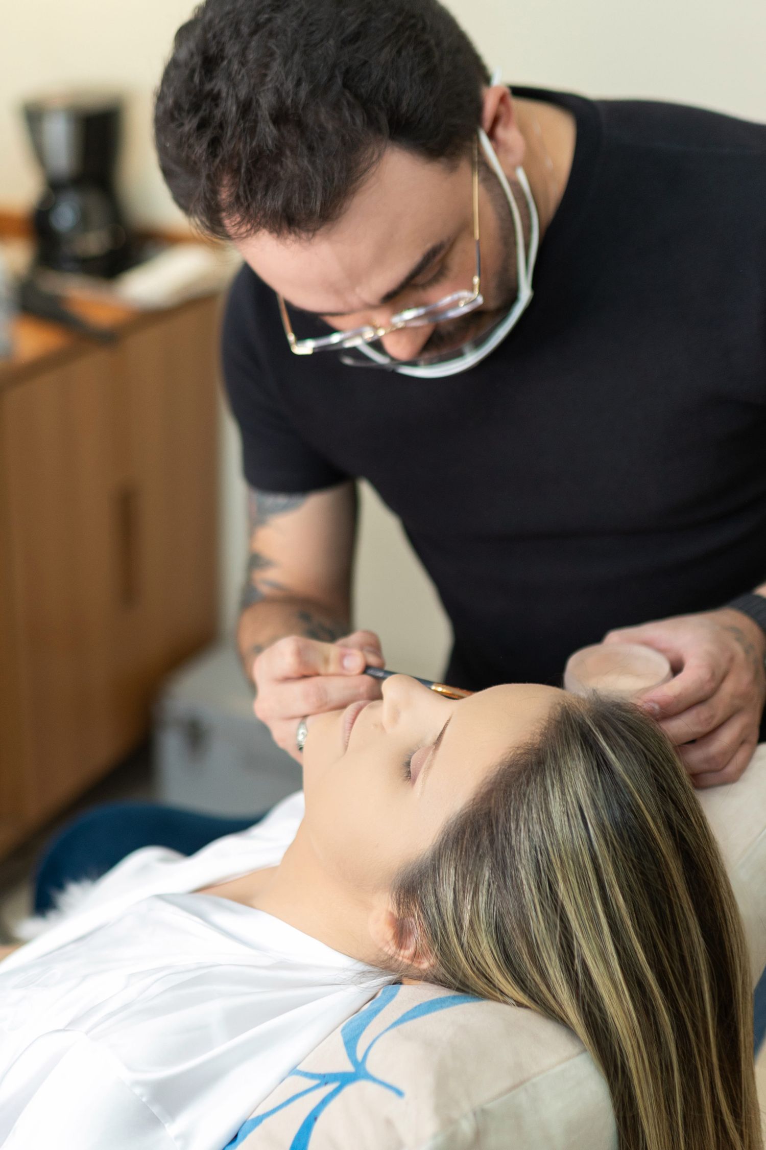 Dentist in black shirt and loupes performing dental procedure on female patient lying in dental chair.