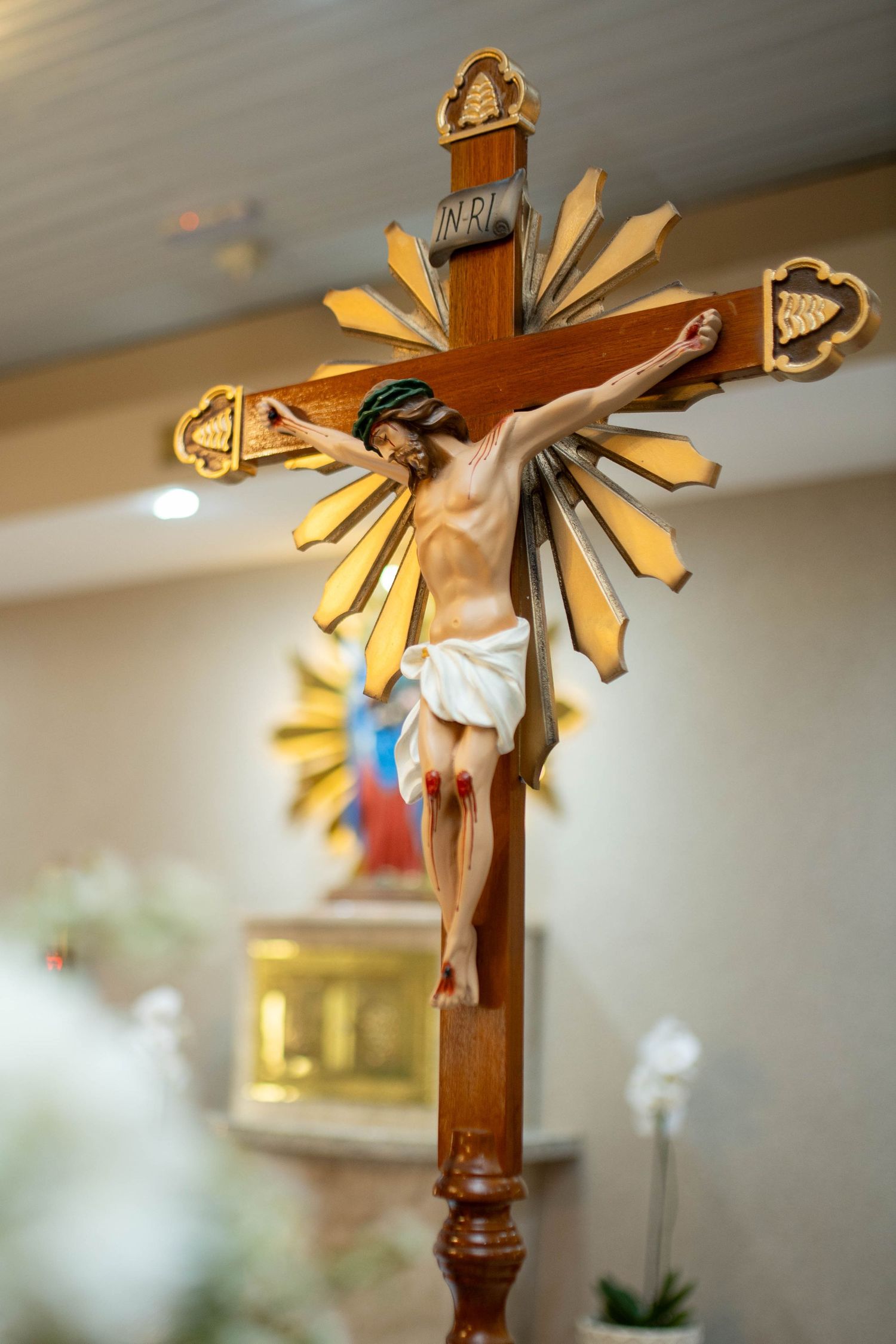 Wooden crucifix with golden sunburst rays and INRI inscription displayed in a Catholic church altar setting.