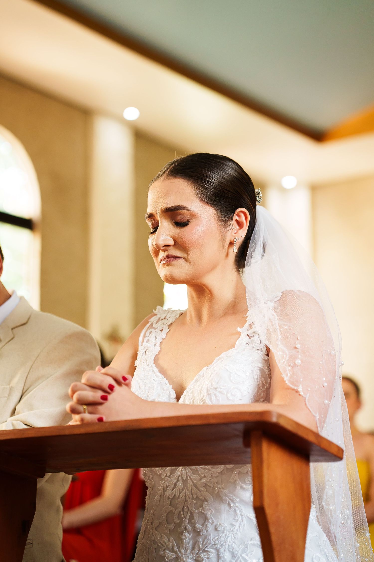 Bride in lace wedding dress and veil praying at altar during church wedding ceremony.