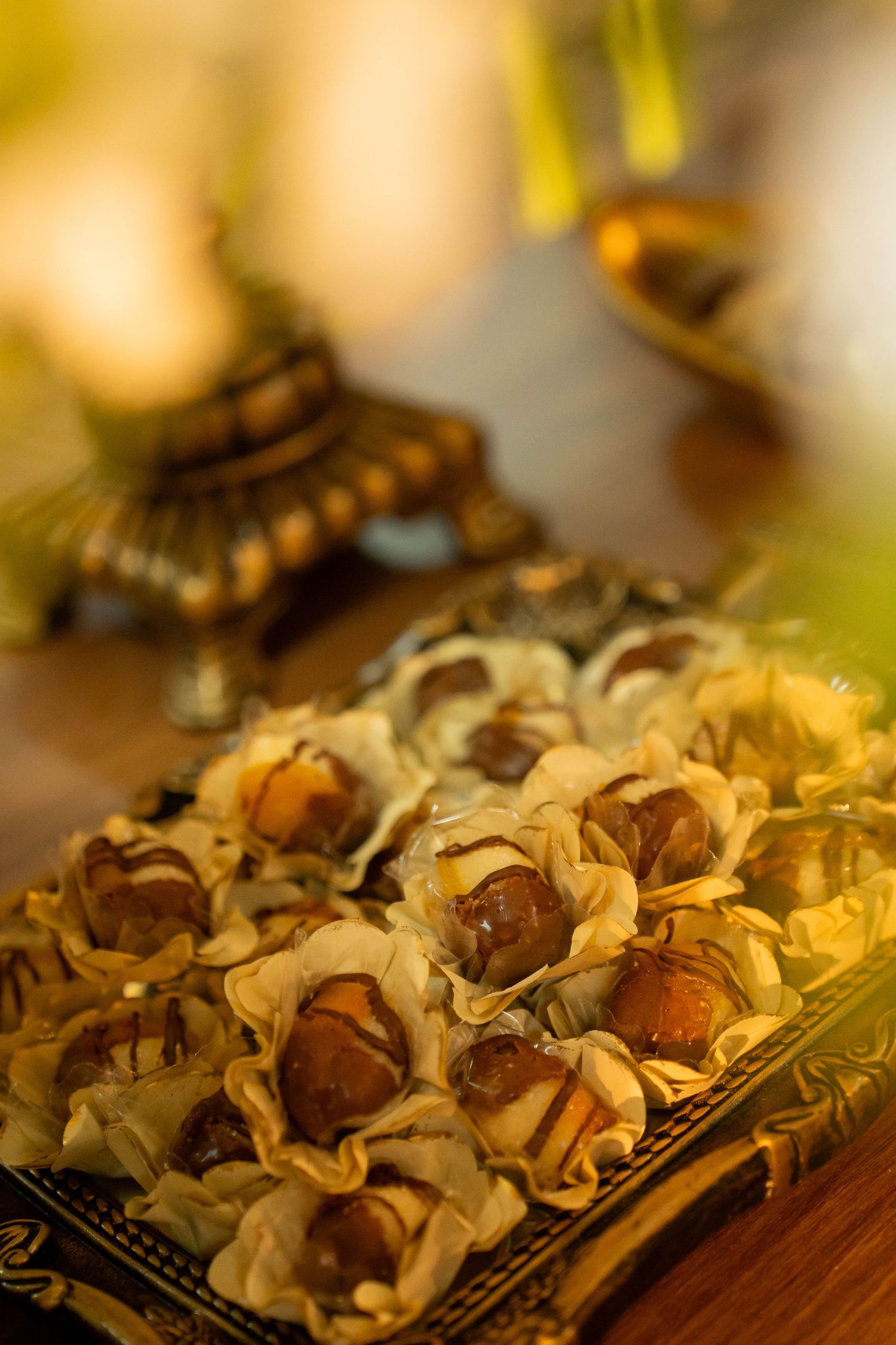 Golden phyllo cups filled with dates and chocolate drizzle on decorative tray at elegant event.