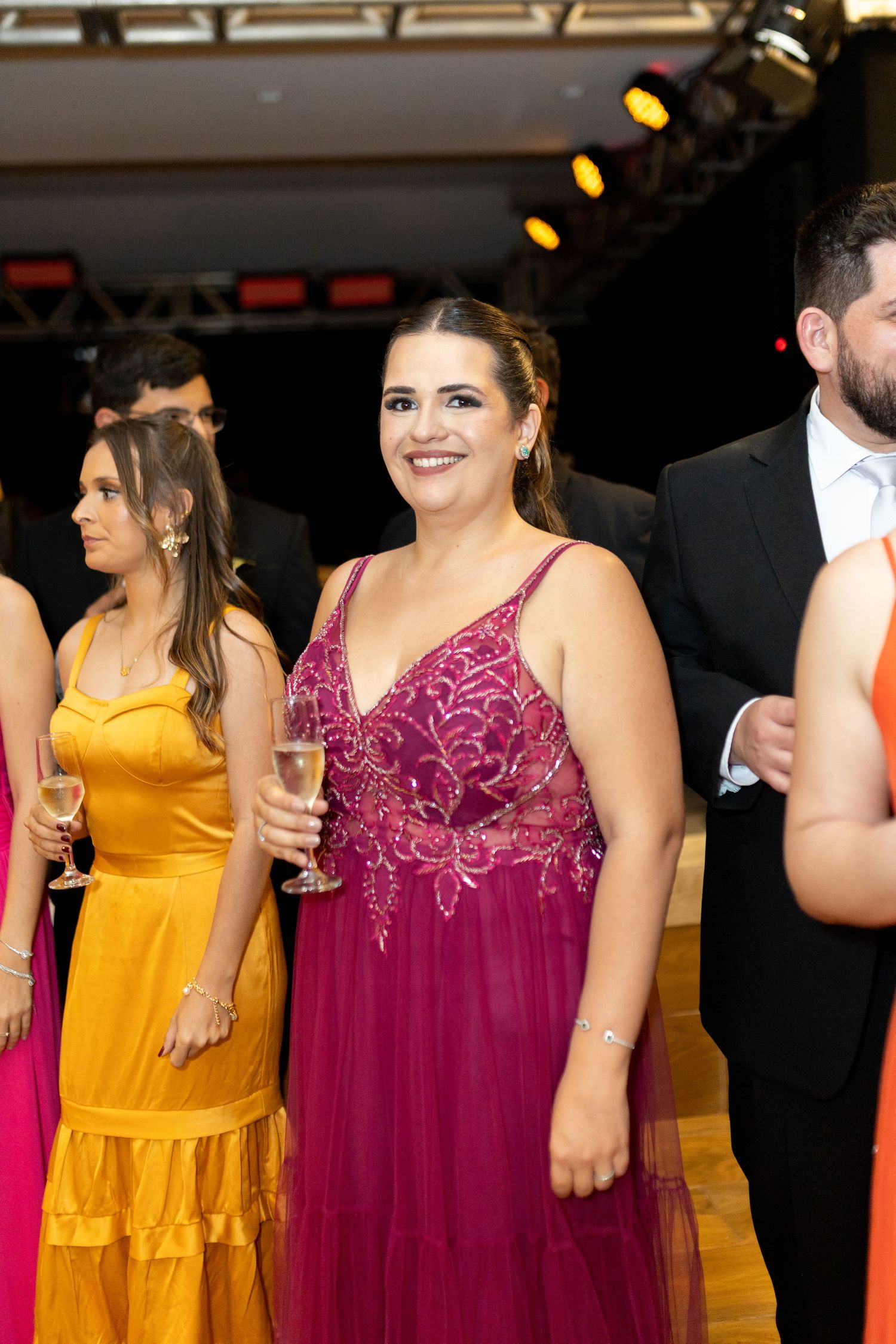 Woman in magenta beaded gown holding champagne glass smiling at formal event.