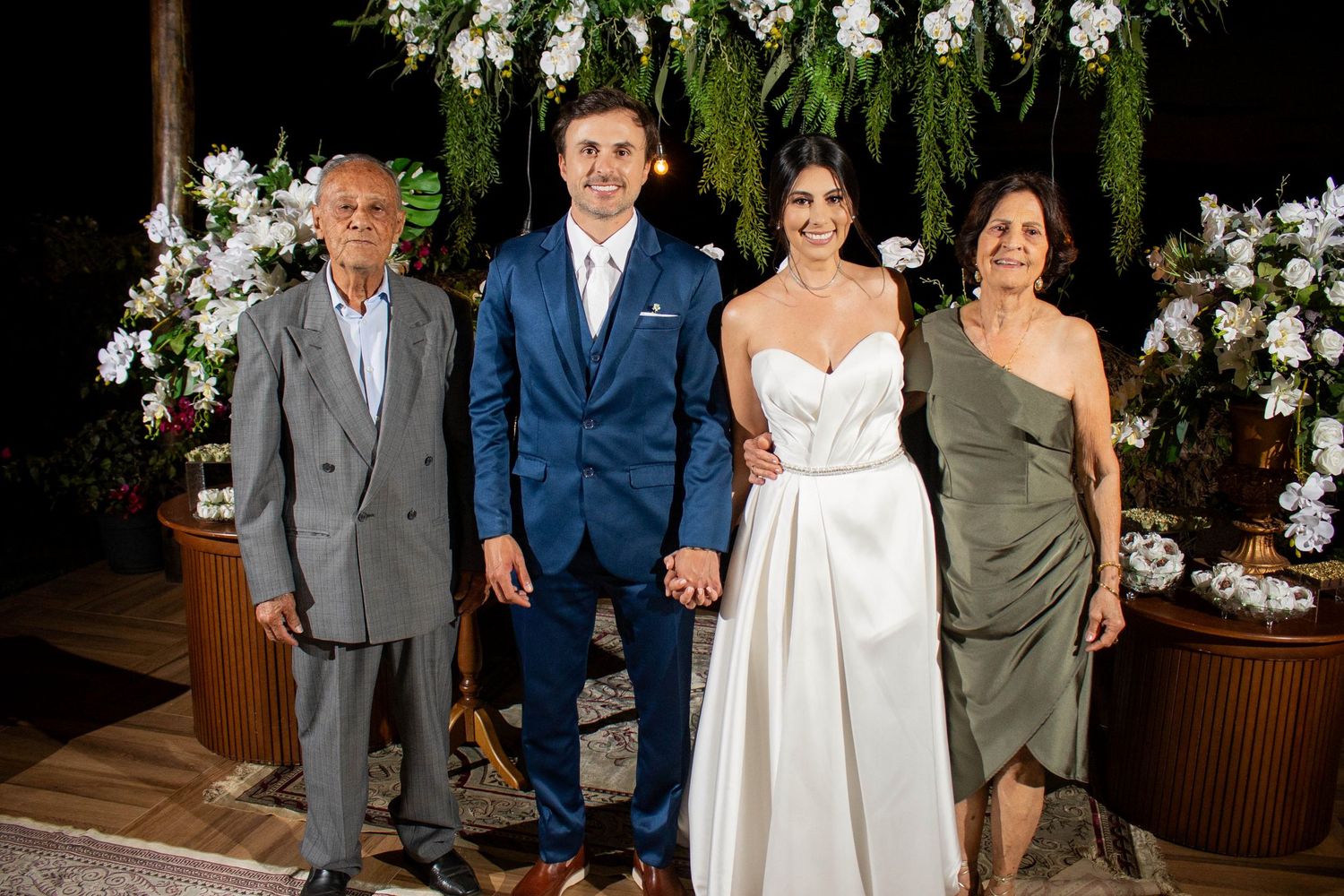 Bride and groom pose with family members at an elegant outdoor wedding reception with floral decorations.