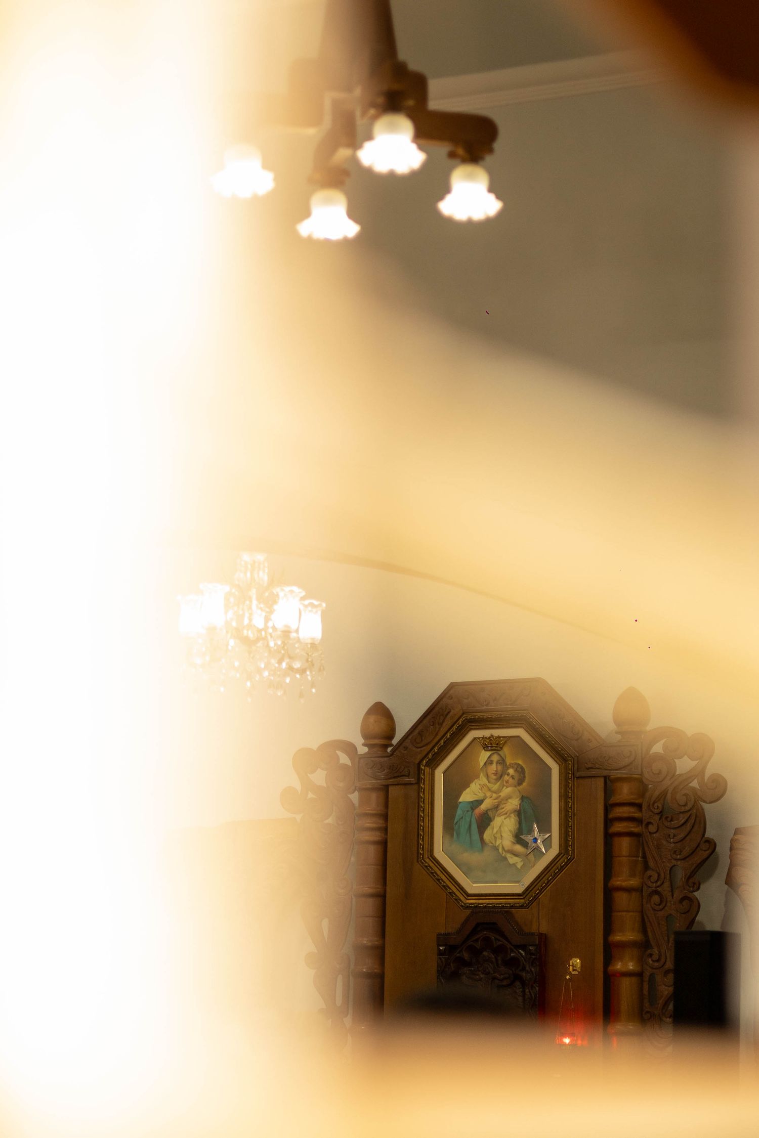 Interior church view with ornate wooden altar, religious painting, and elegant chandeliers in warm golden light.