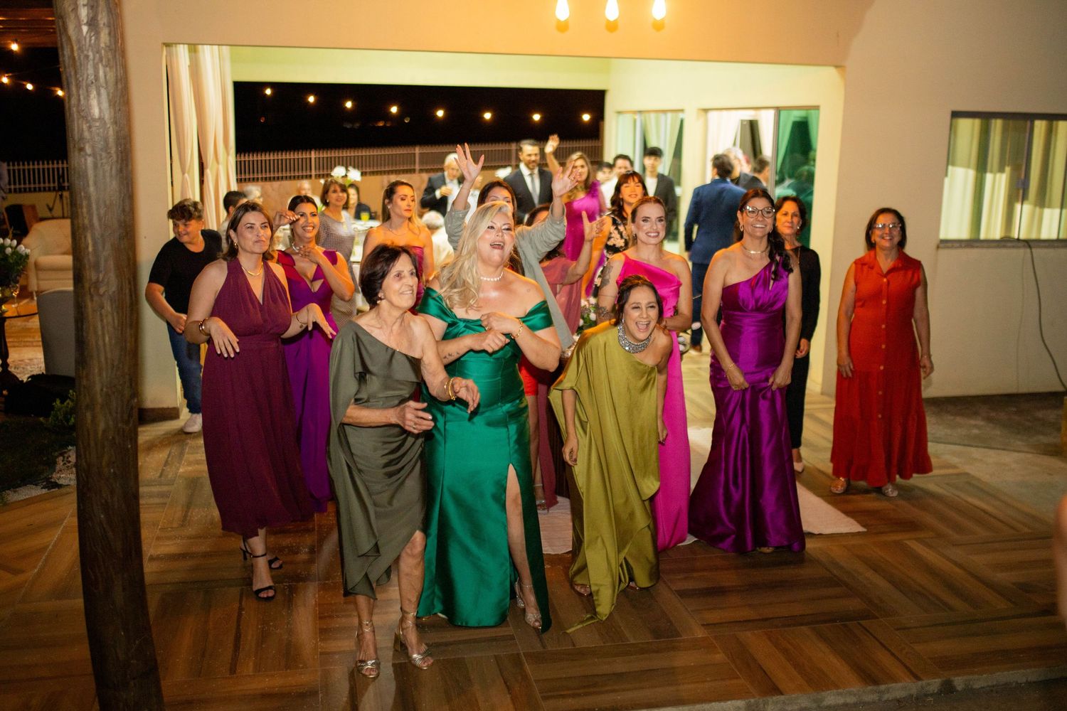 Group of elegantly dressed women in colorful gowns posing together at a formal evening event or wedding reception.