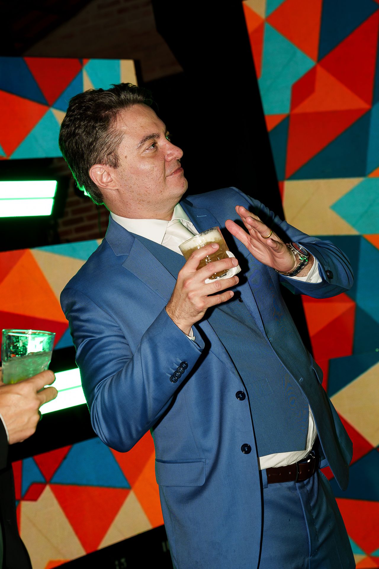 Man in blue suit holding a beer glass at a colorful geometric patterned party event.