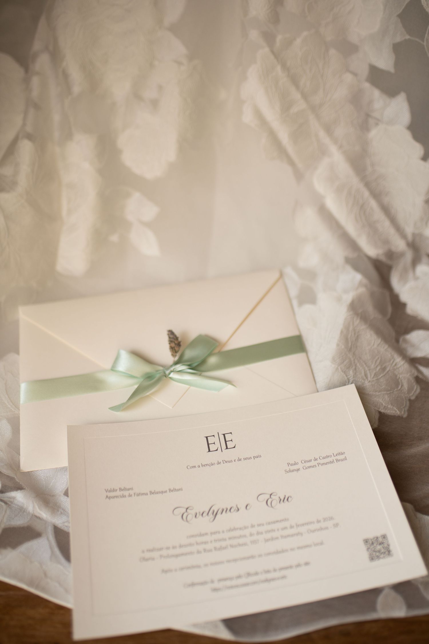 Elegant wedding invitation with mint green ribbon bow and butterfly detail on ivory envelope, displayed on lace fabric.