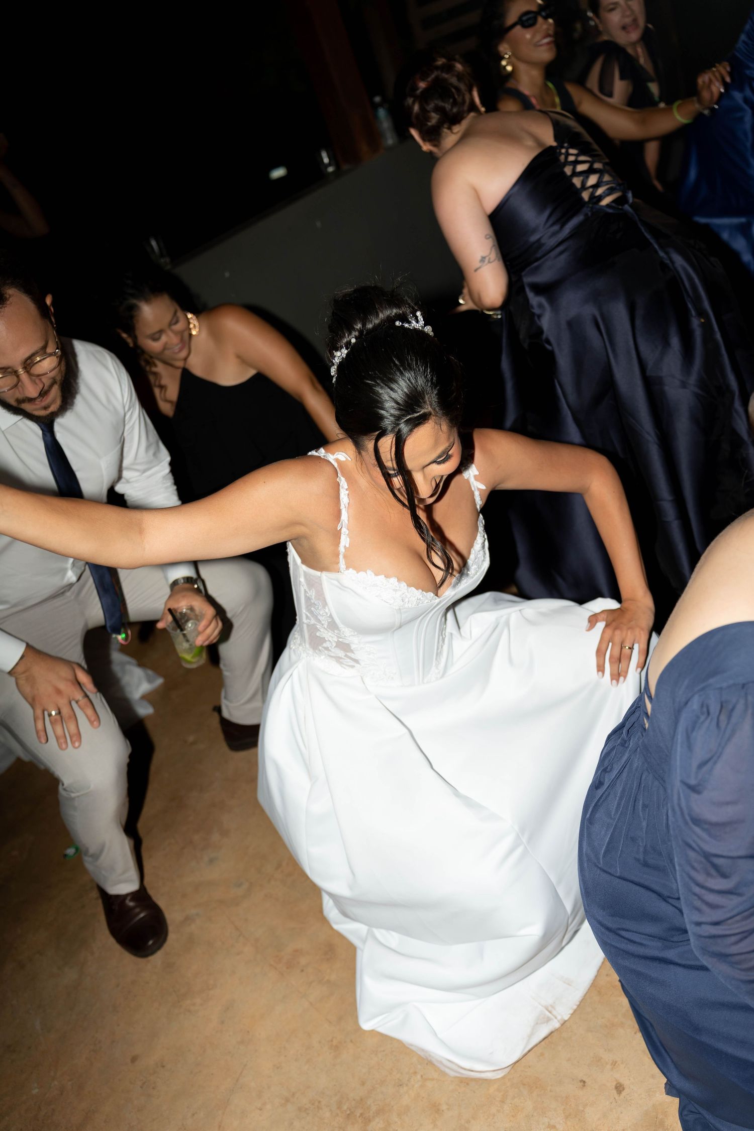 Bride in white wedding gown dancing energetically with guests at wedding reception celebration.