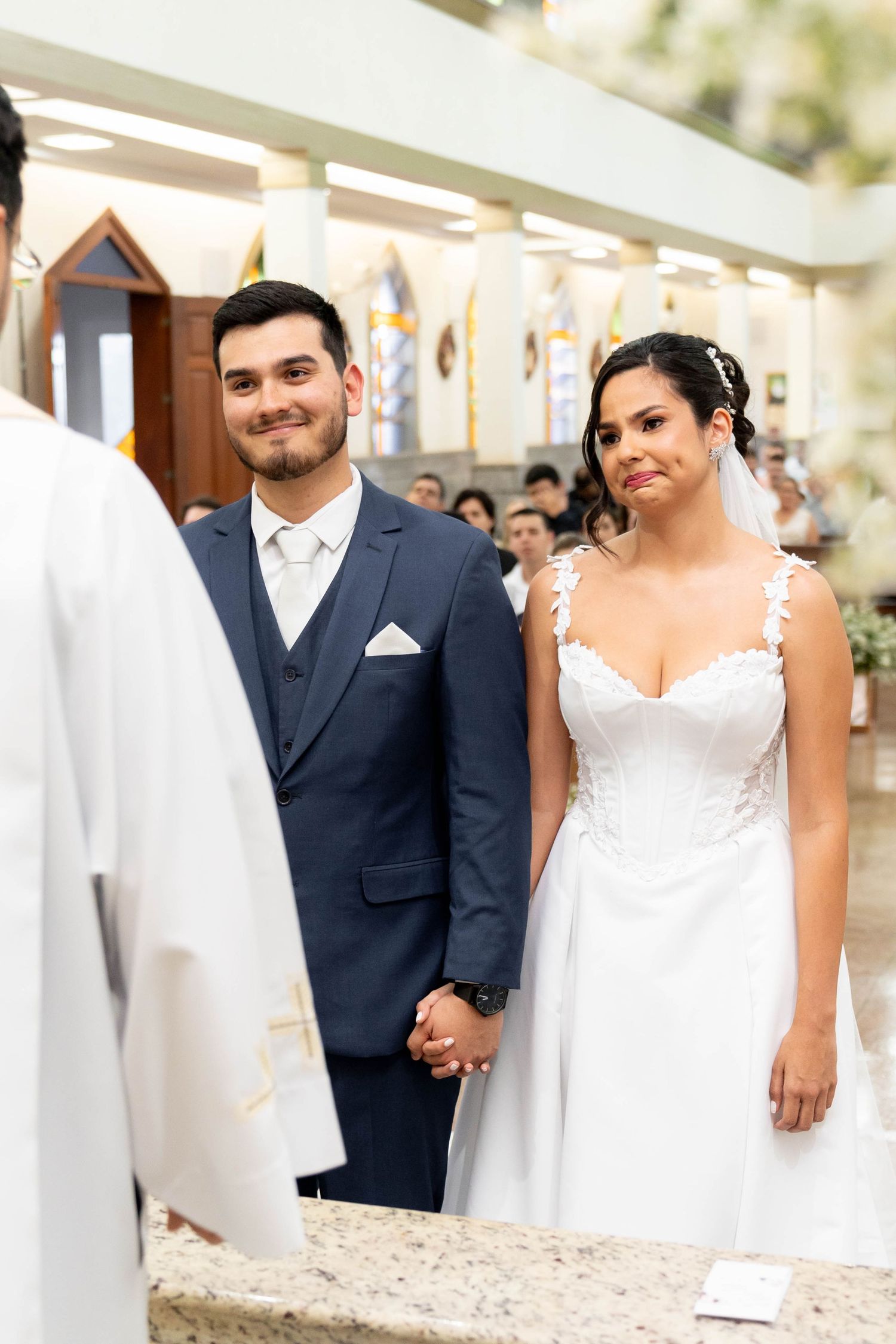 A bride and groom hold hands at the altar during their church wedding ceremony, smiling at the officiant.