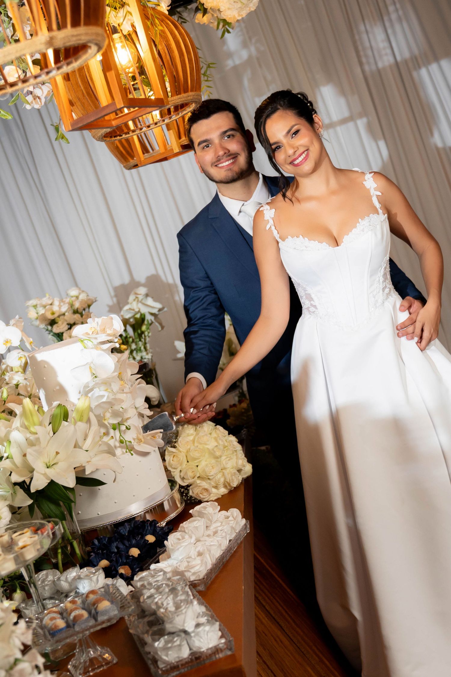 Smiling bride and groom cutting their elegant white wedding cake at a beautifully decorated reception table.