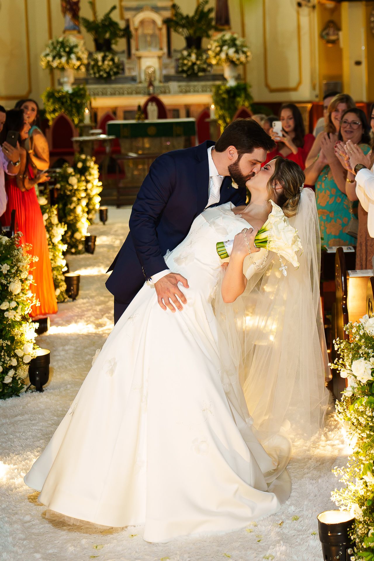 Bride and groom share a romantic dip kiss in a beautifully decorated church aisle after their wedding ceremony.