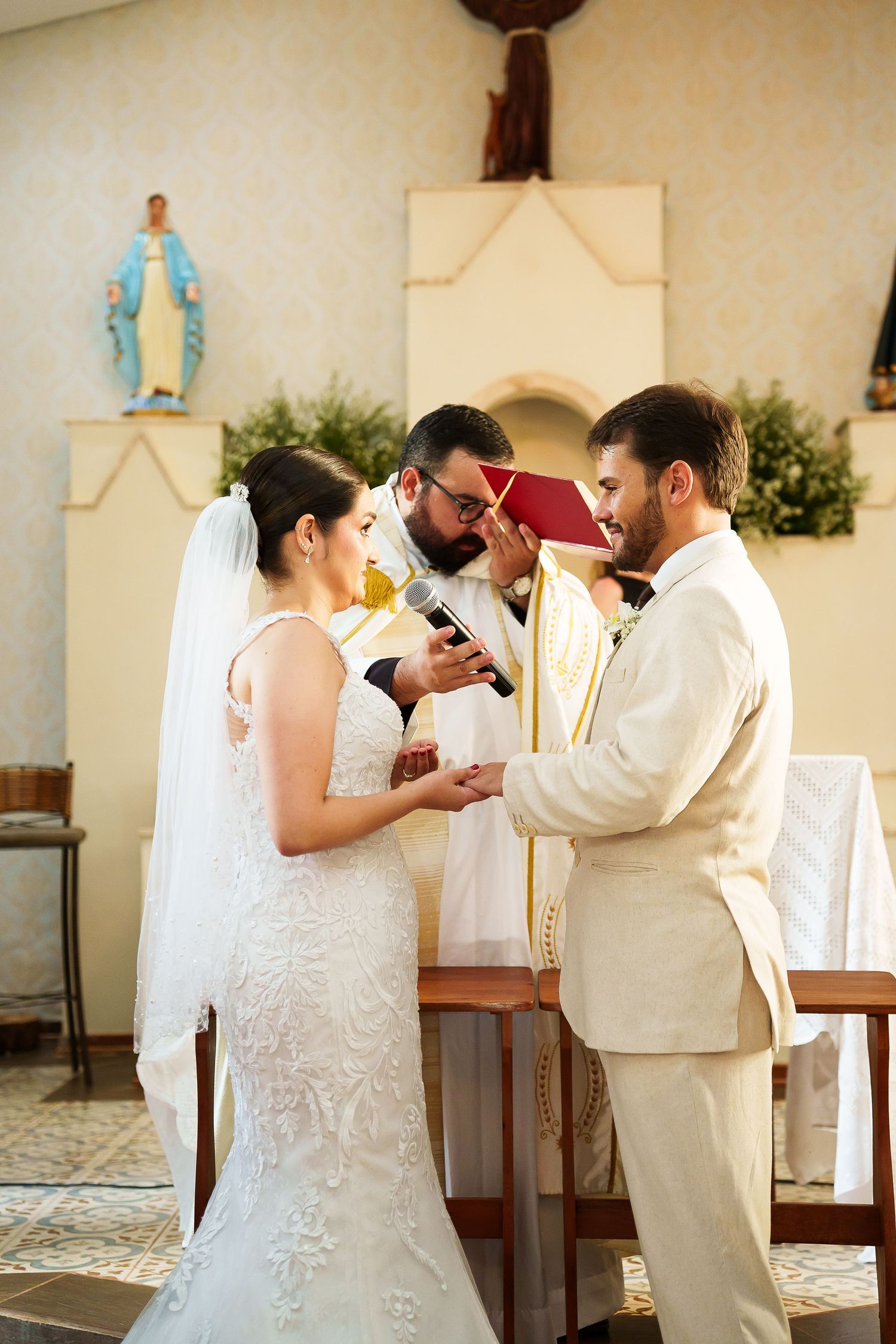 Bride and groom exchange rings during a Catholic church wedding ceremony with priest officiating.