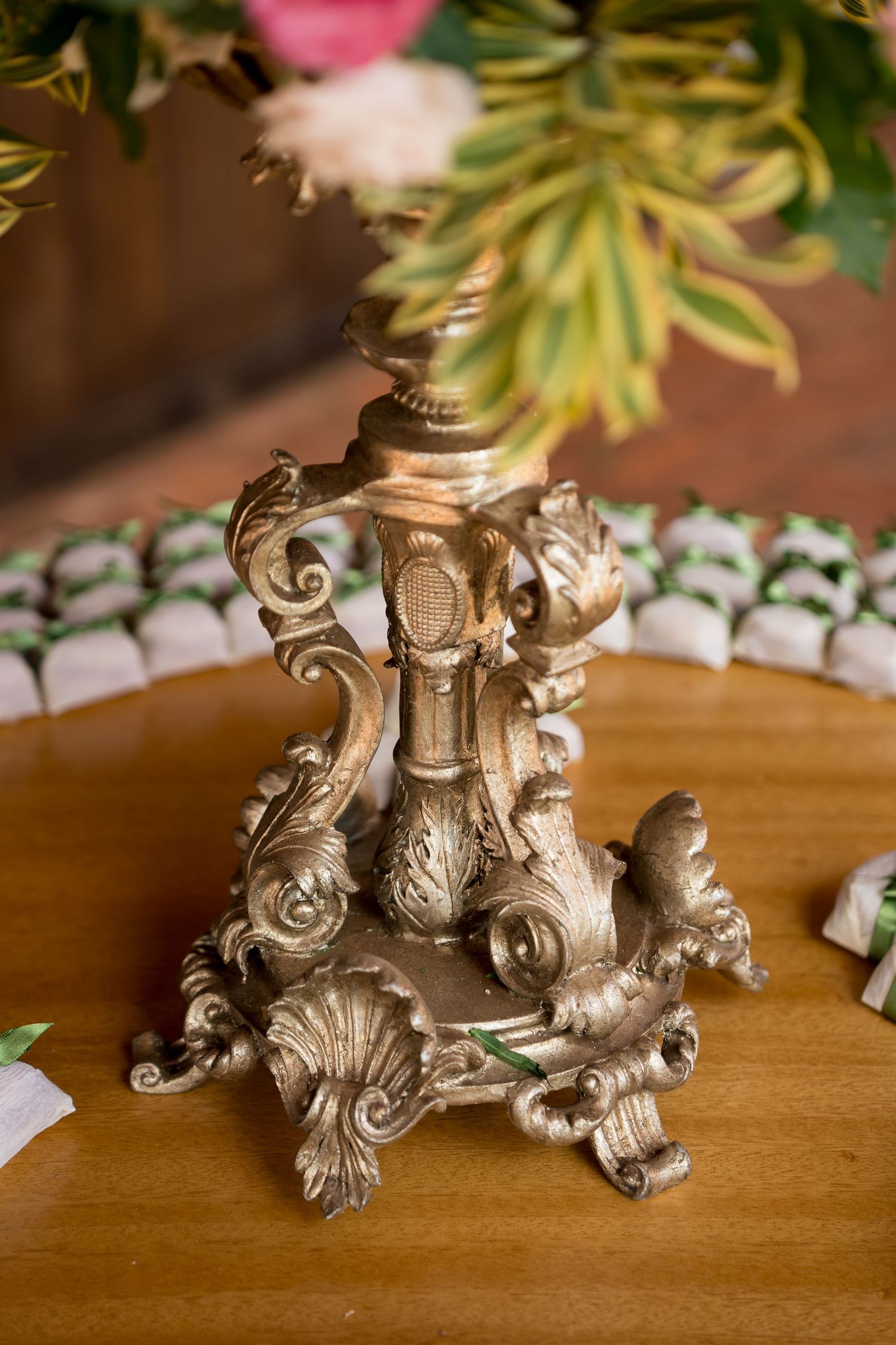 Ornate gold baroque candlestick holder on wooden table with floral arrangement and decorative place cards in background.