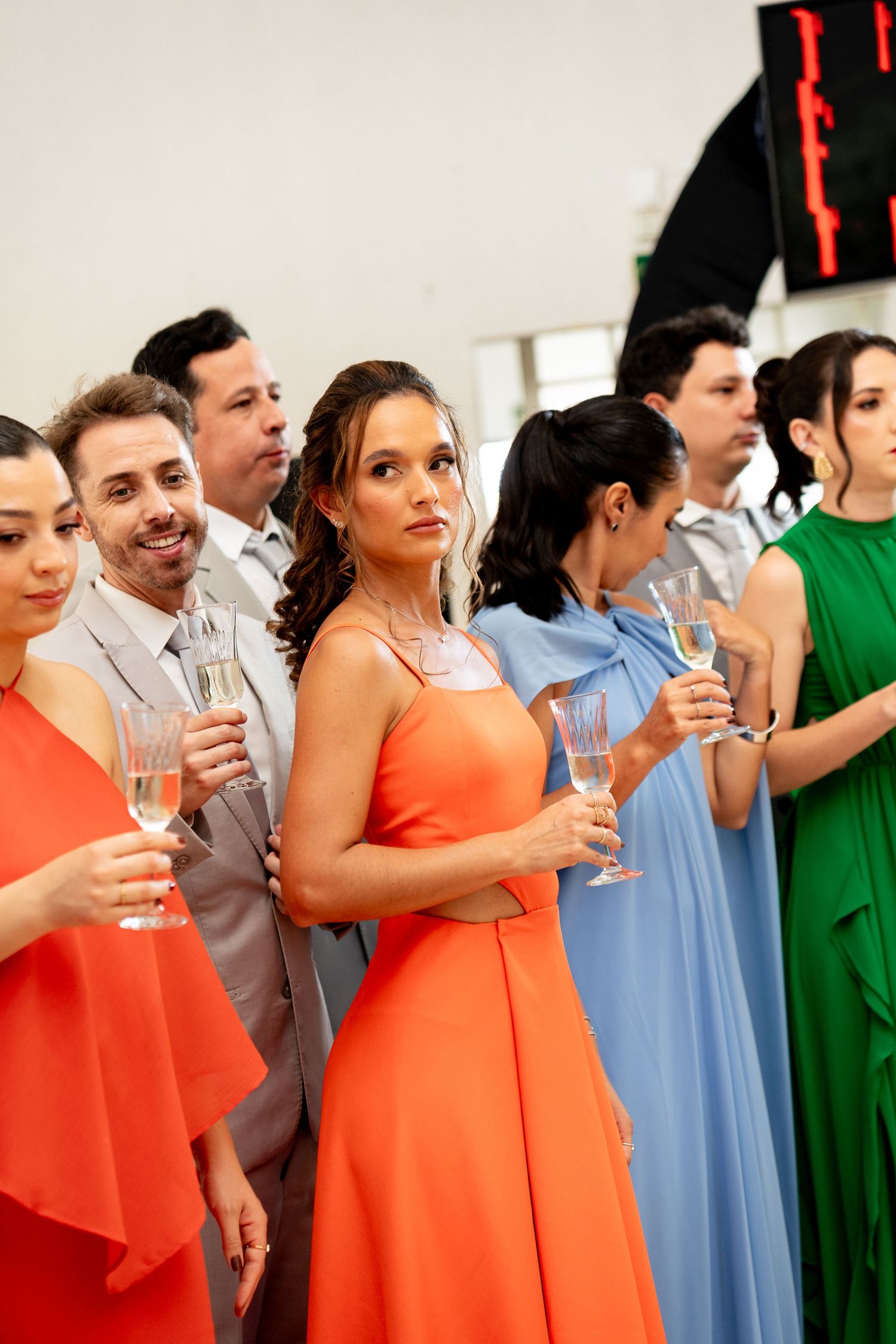 Elegantly dressed guests in colorful gowns holding champagne glasses at a formal celebration event.
