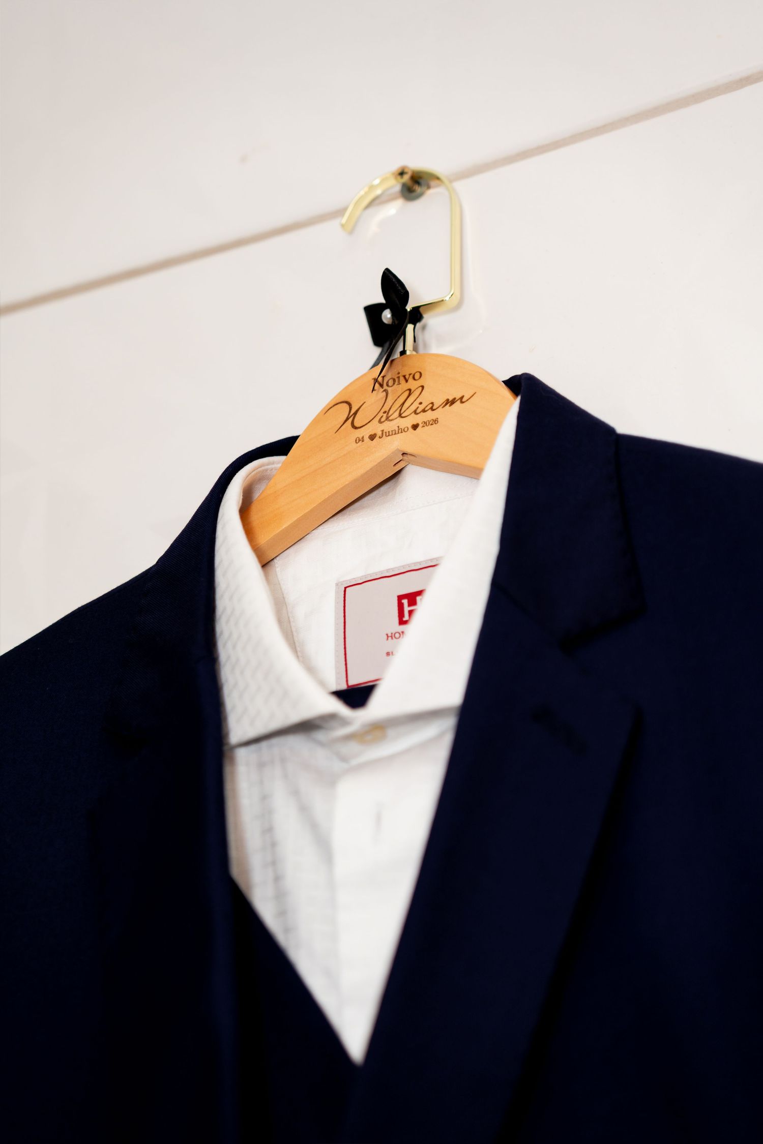 Navy blue suit jacket and white dress shirt on a personalized wooden hanger against a white wall.