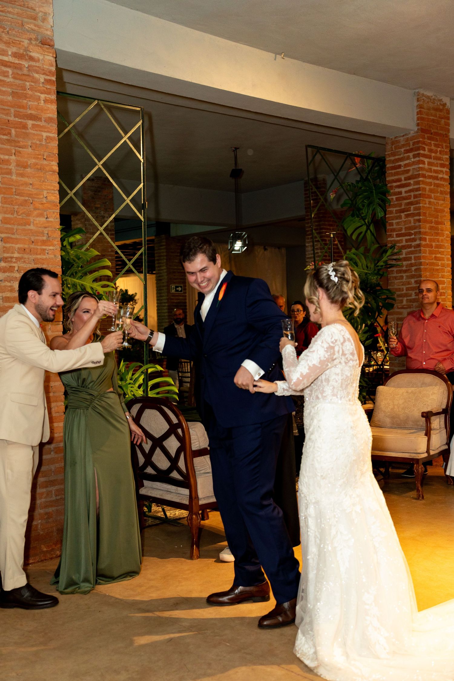 Bride and groom toasting champagne with guests in elegant wedding venue with brick walls and tropical decor.