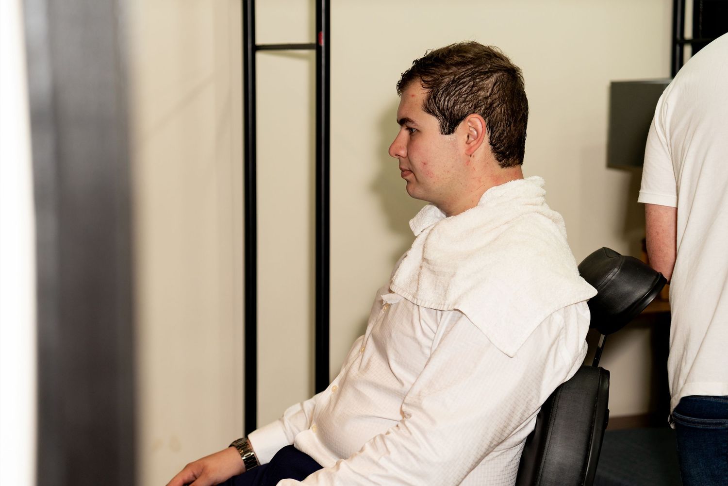 Man in white jacket sitting in chair at desk, viewed from side profile in modern office setting.