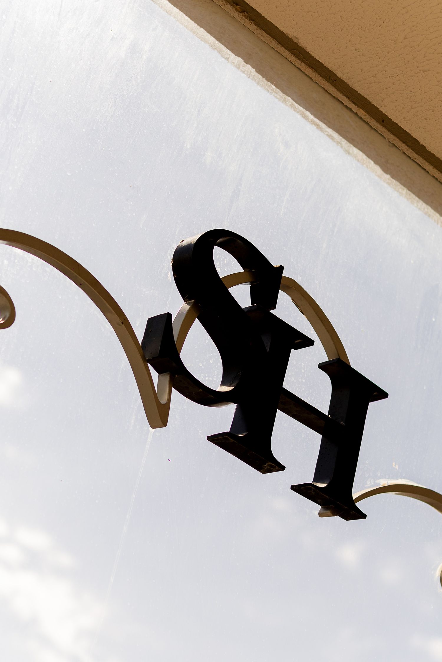 Black ornate metal SH monogram sign mounted on a decorative wrought iron bracket against a white wall.
