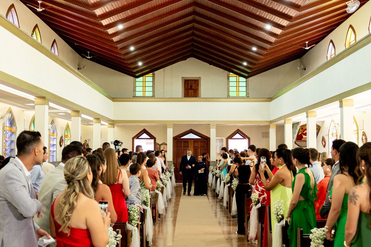 Elegant church wedding ceremony with guests in colorful formal attire lining the aisle.