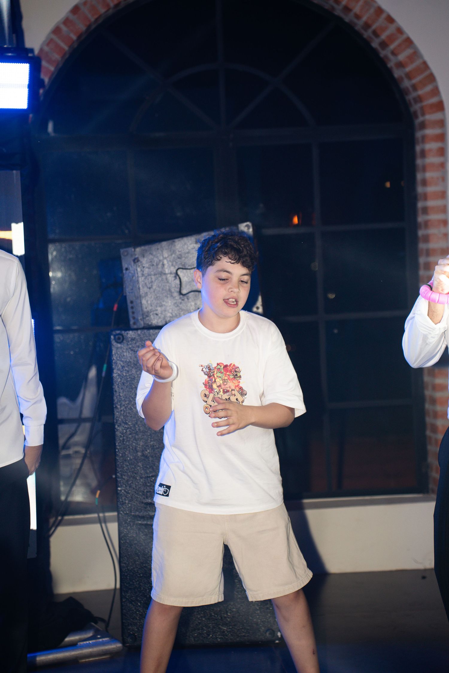 Young boy in white t-shirt and beige shorts dancing energetically at an indoor party event.