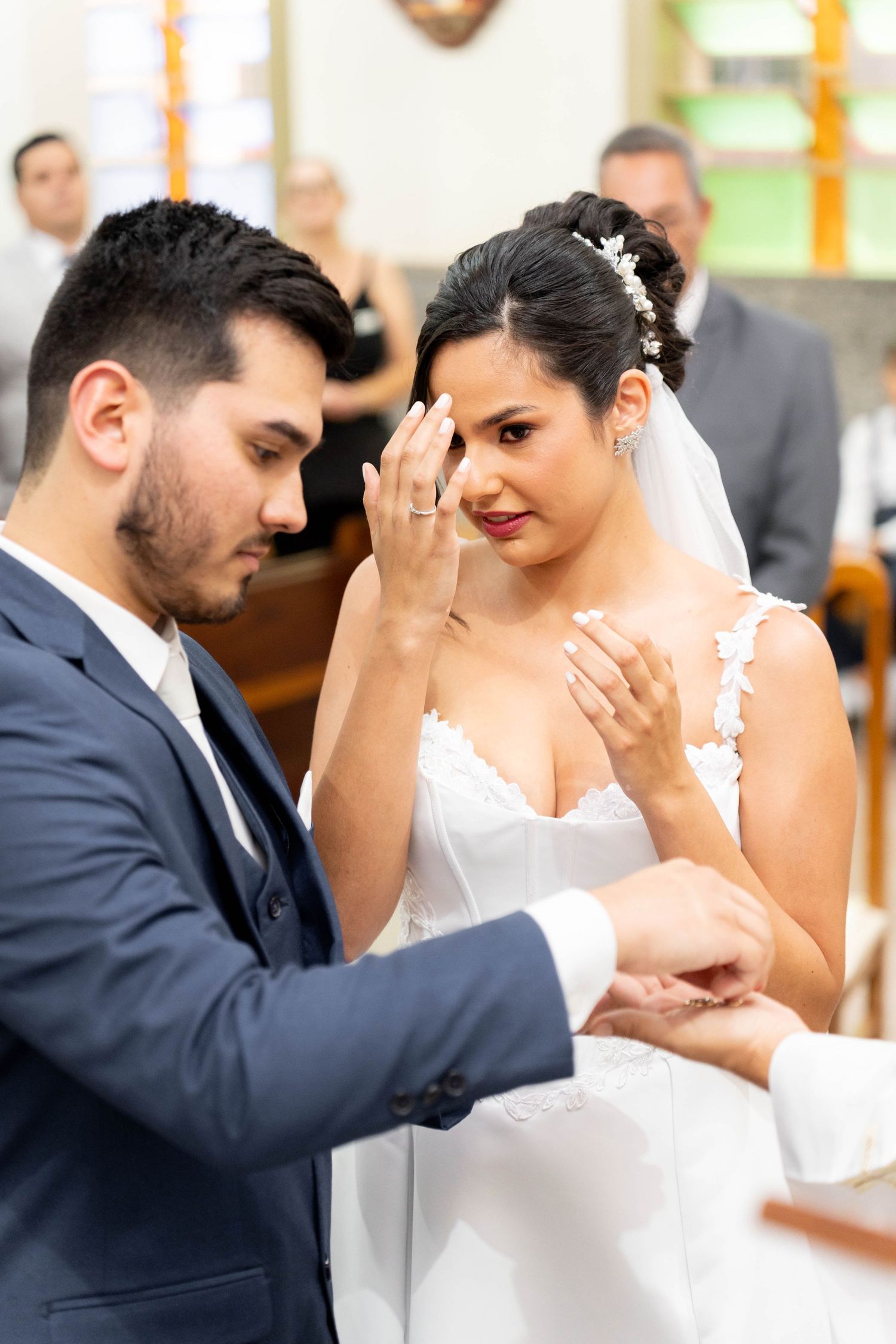 Emotional bride wiping tears as groom places wedding ring on her finger during church ceremony.