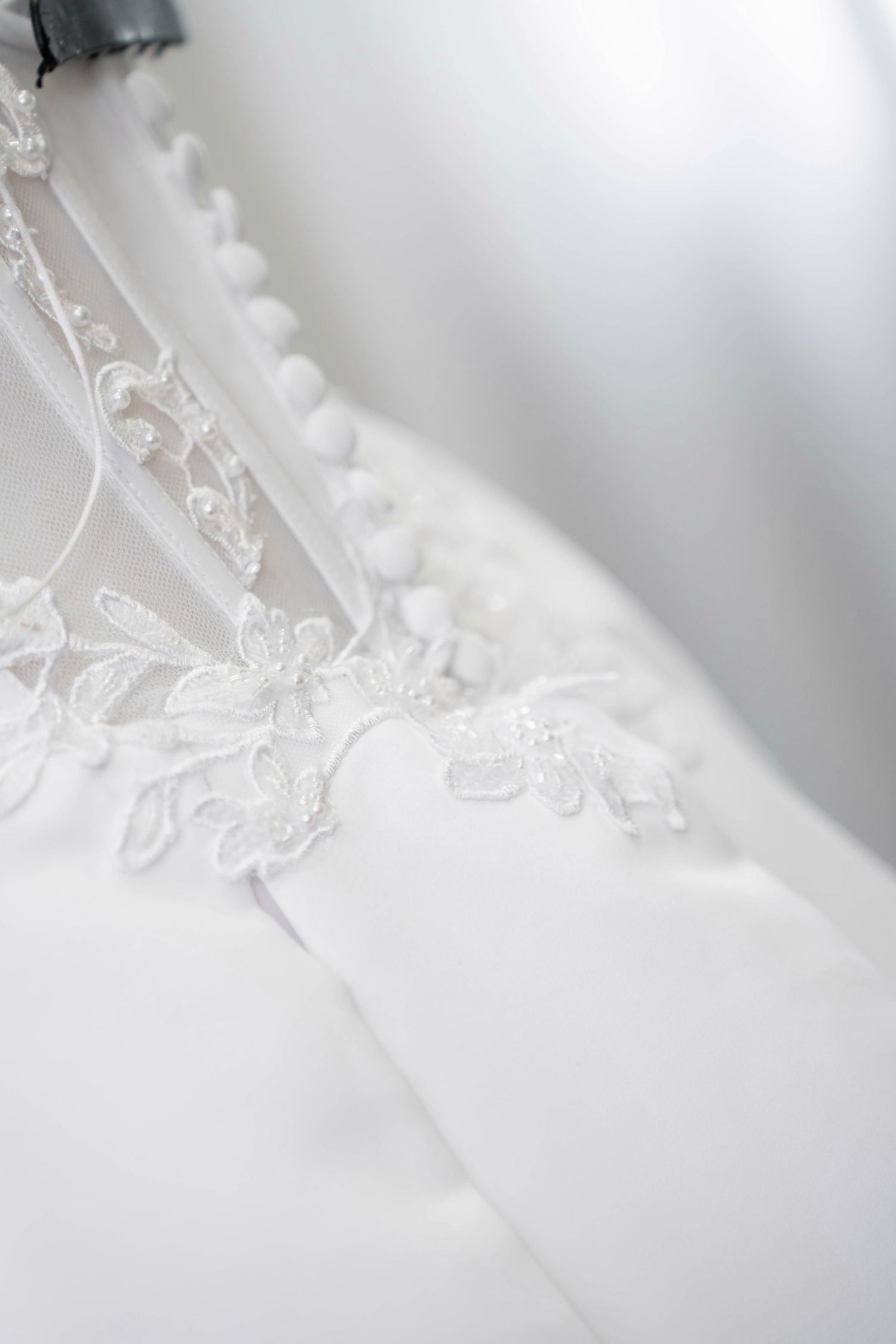 Close-up of elegant white wedding dress featuring delicate lace floral embroidery and pearl button details on corset back.