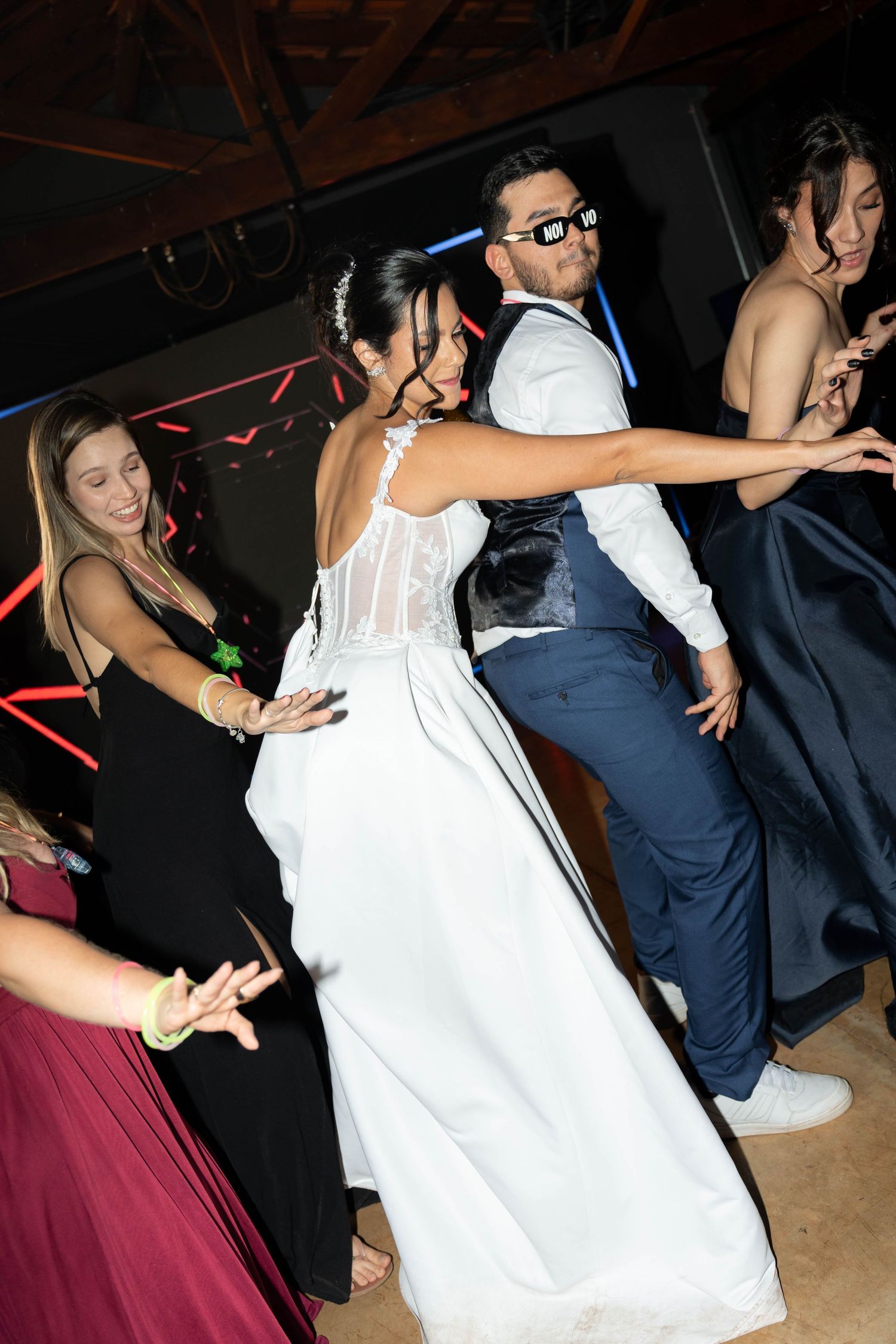 Bride and groom dancing together at wedding reception surrounded by guests in formal attire on a festive dance floor.