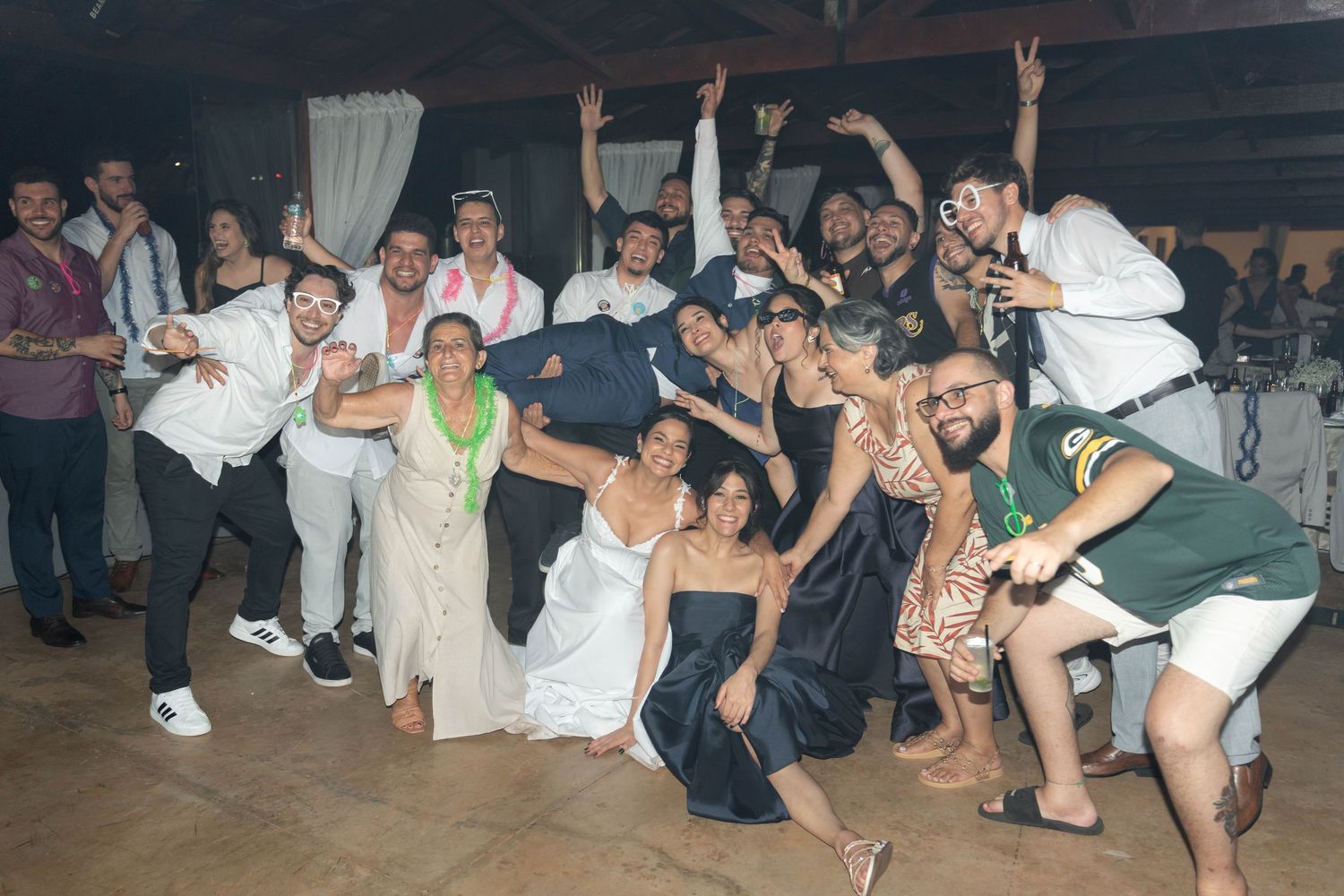 Large wedding reception group photo with guests celebrating, dancing, and posing joyfully in a decorated indoor venue.
