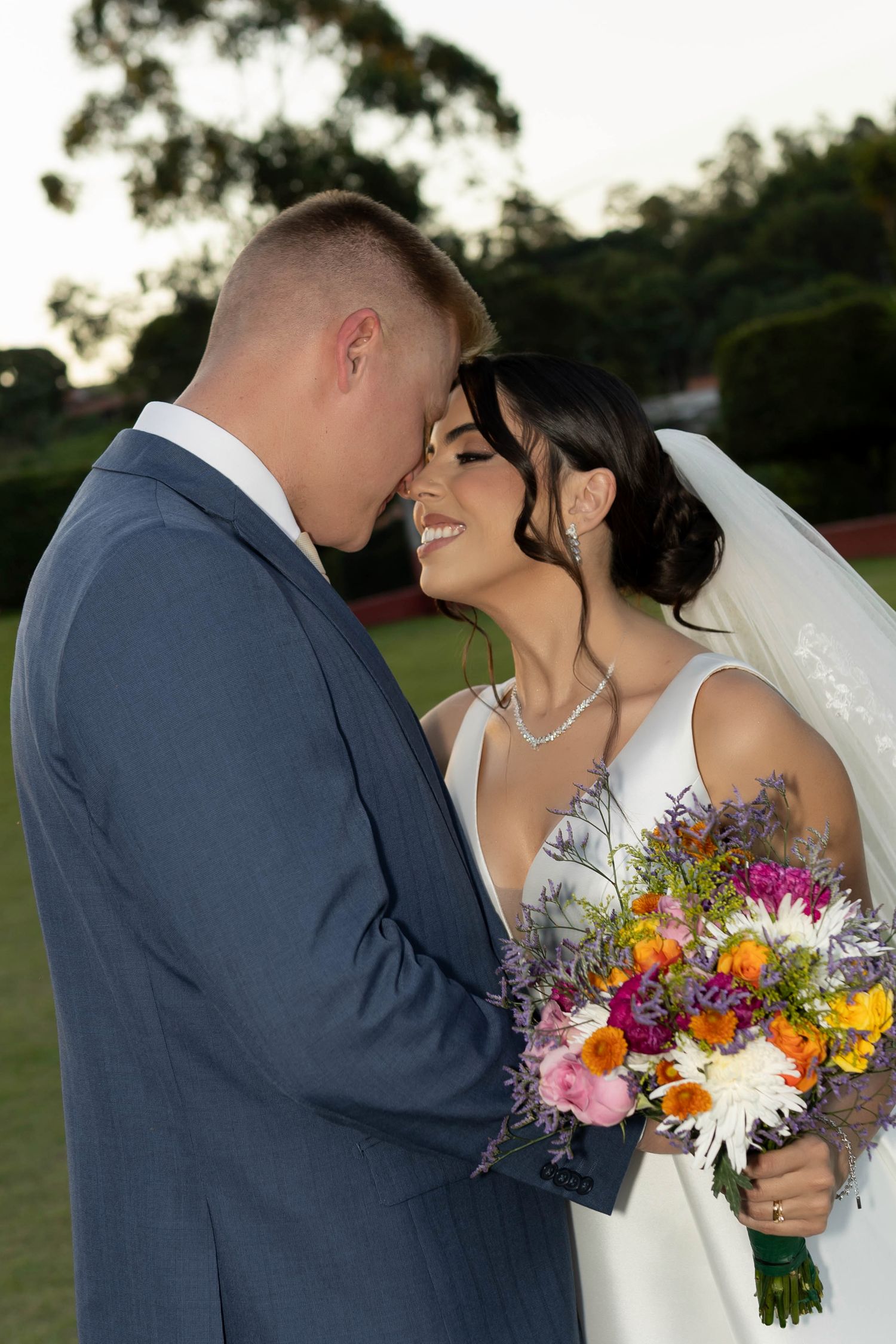 Bride and groom sharing a romantic moment outdoors, bride holding a vibrant colorful bouquet in a white wedding dress.