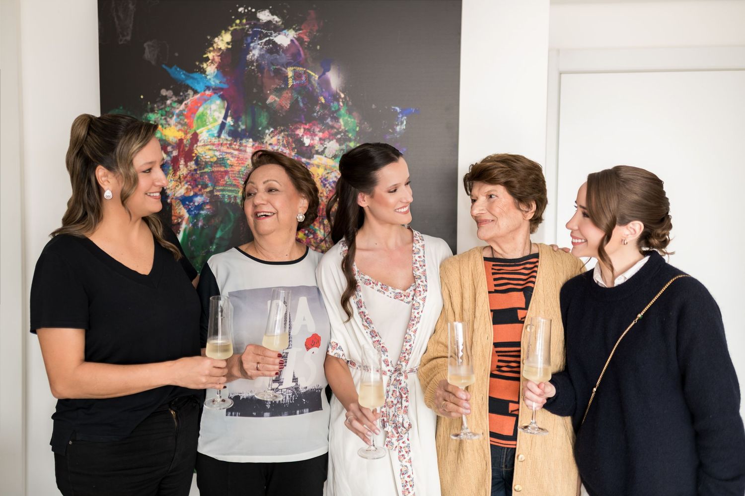 Five women laughing and toasting with champagne glasses at an art gallery event.
