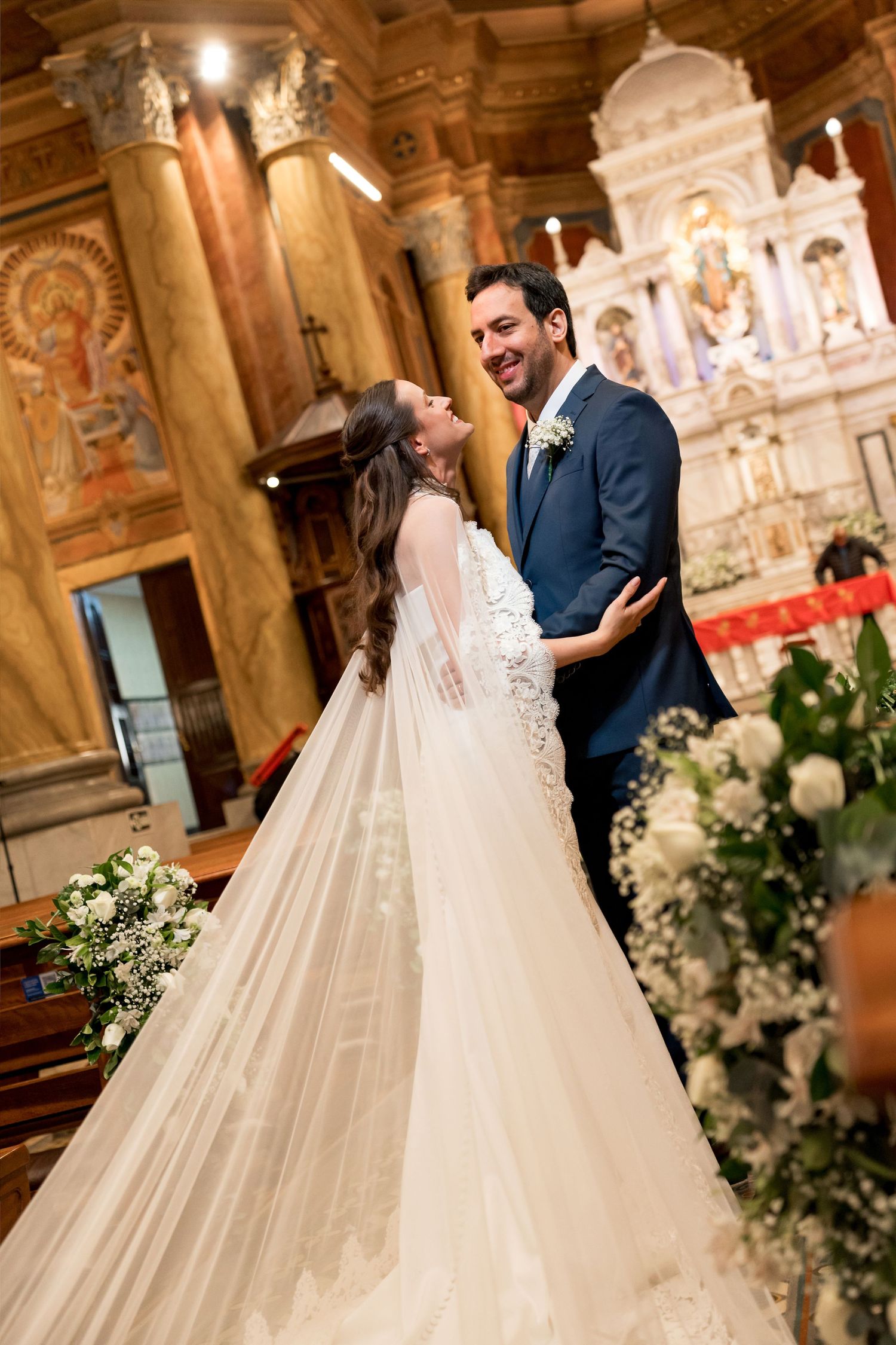 A joyful bride and groom share a romantic moment at the church altar, she in a flowing white gown with veil.