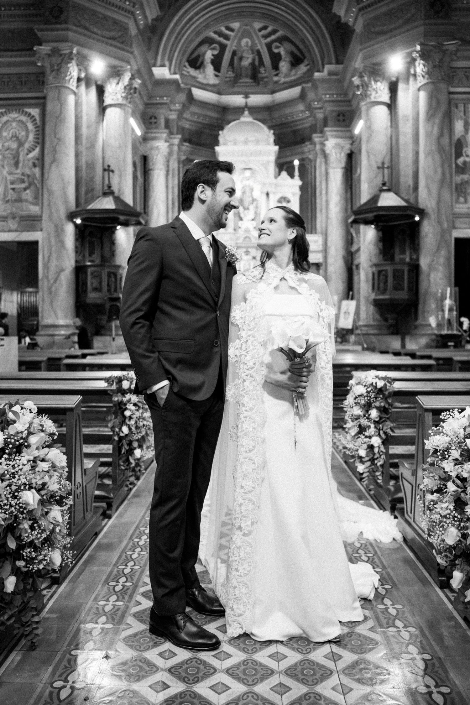Black and white photo of a bride and groom sharing a romantic moment in an ornate church aisle.