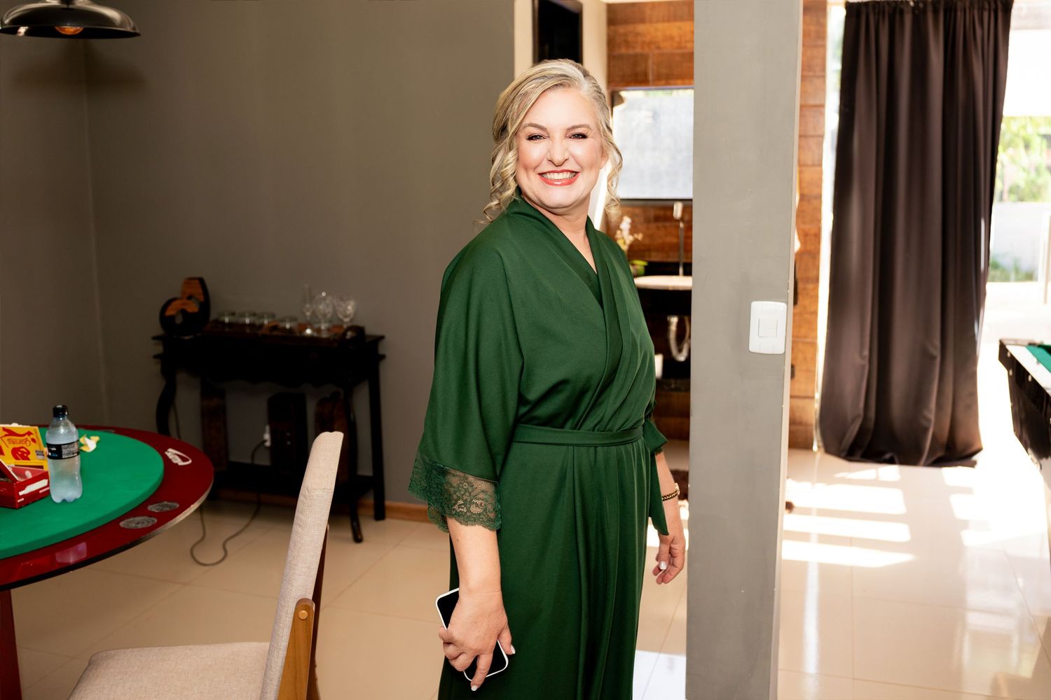 Woman in elegant green satin robe smiling indoors, posing in a modern living space with warm lighting.