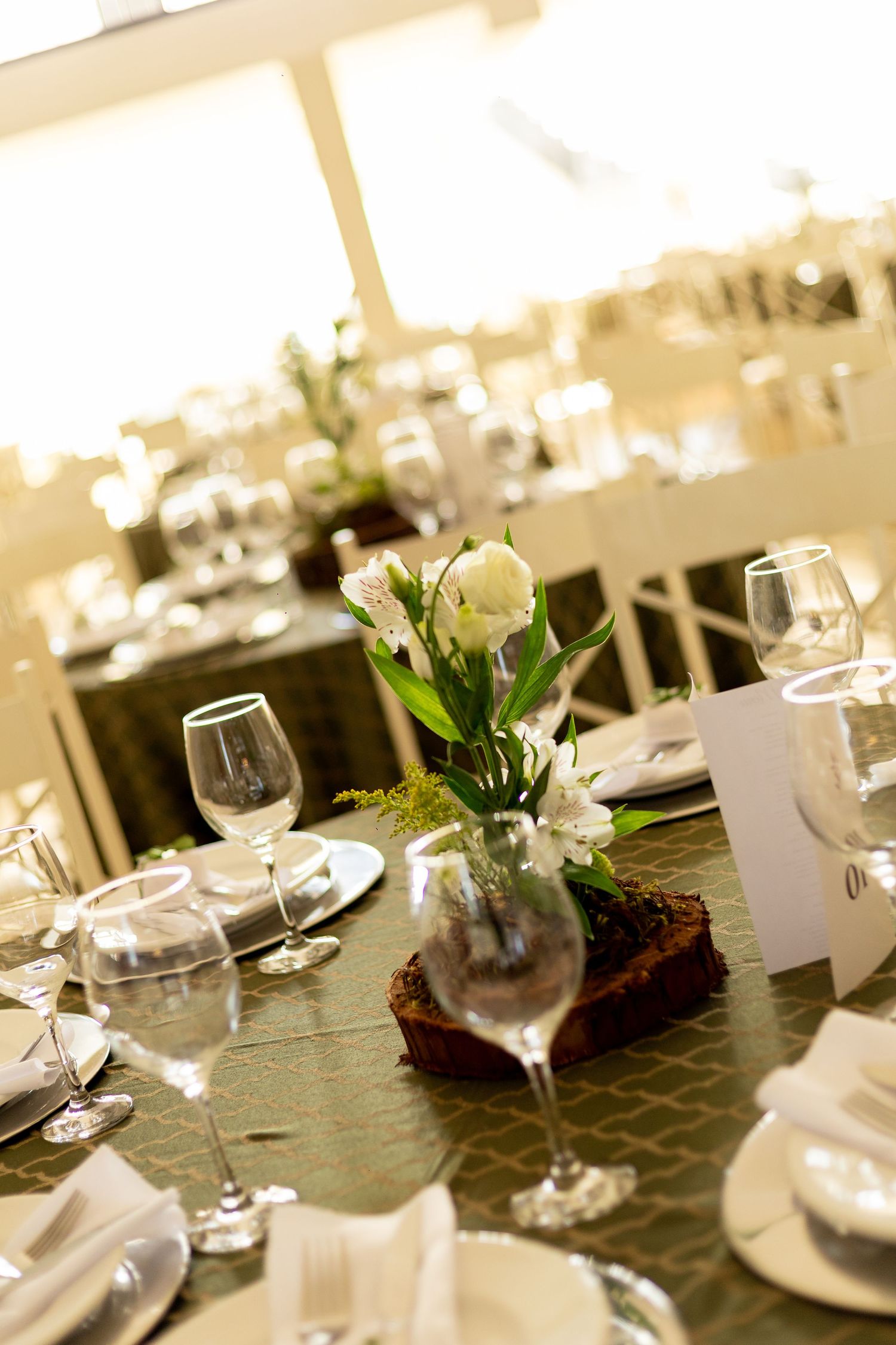 Elegant wedding reception table set with crystal wine glasses, white floral centerpiece, and neatly folded napkins on green tablecloth.