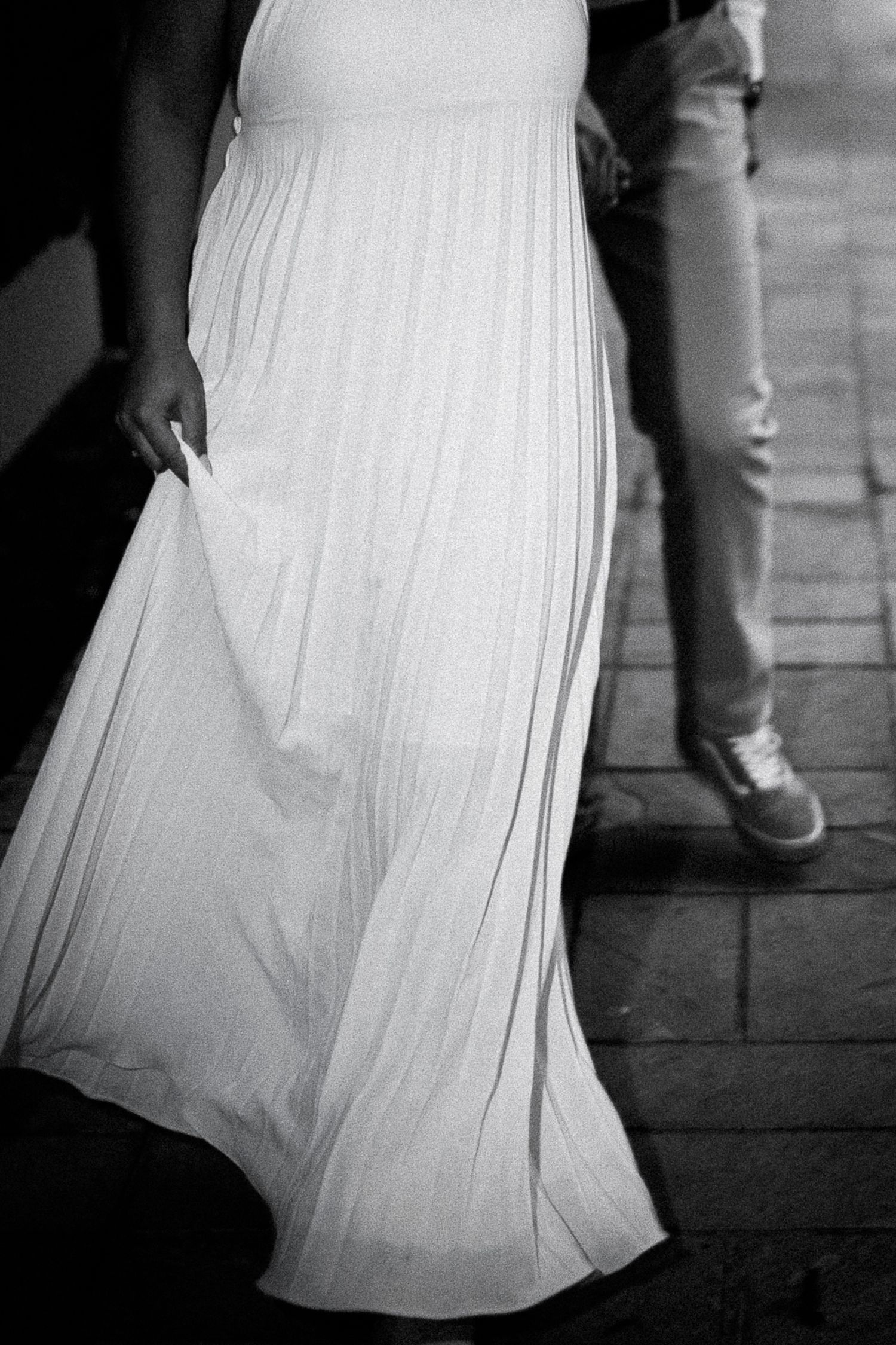 Black and white photo of a woman in a flowing white maxi dress walking on a cobblestone path.