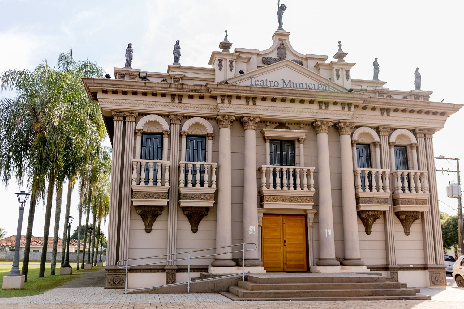Historic neoclassical Teatro Municipal theater building with ornate facade, balcony, statues, and wooden doors in Brazil.