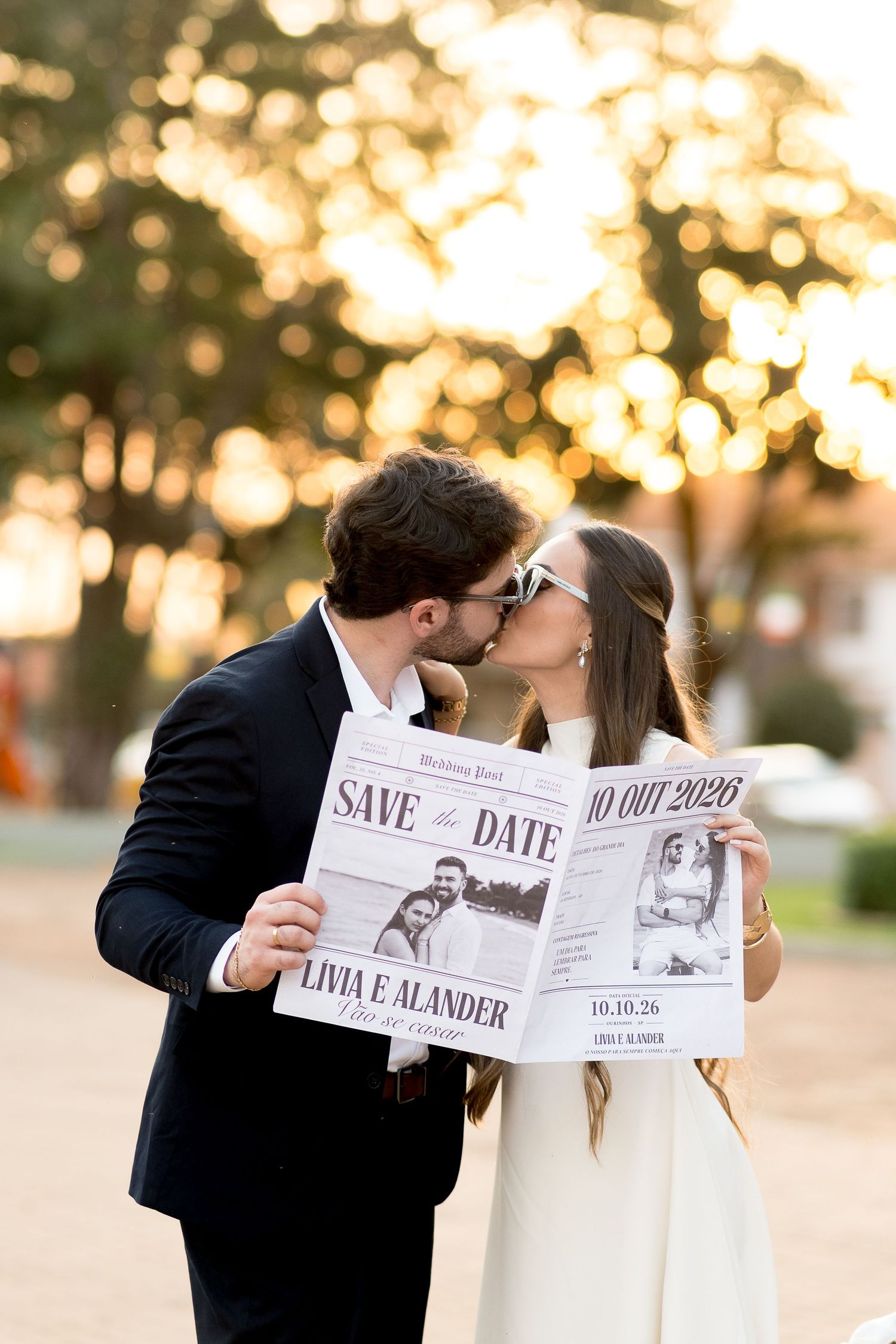 Couple kissing behind Save the Date newspaper announcement with golden bokeh background at sunset.
