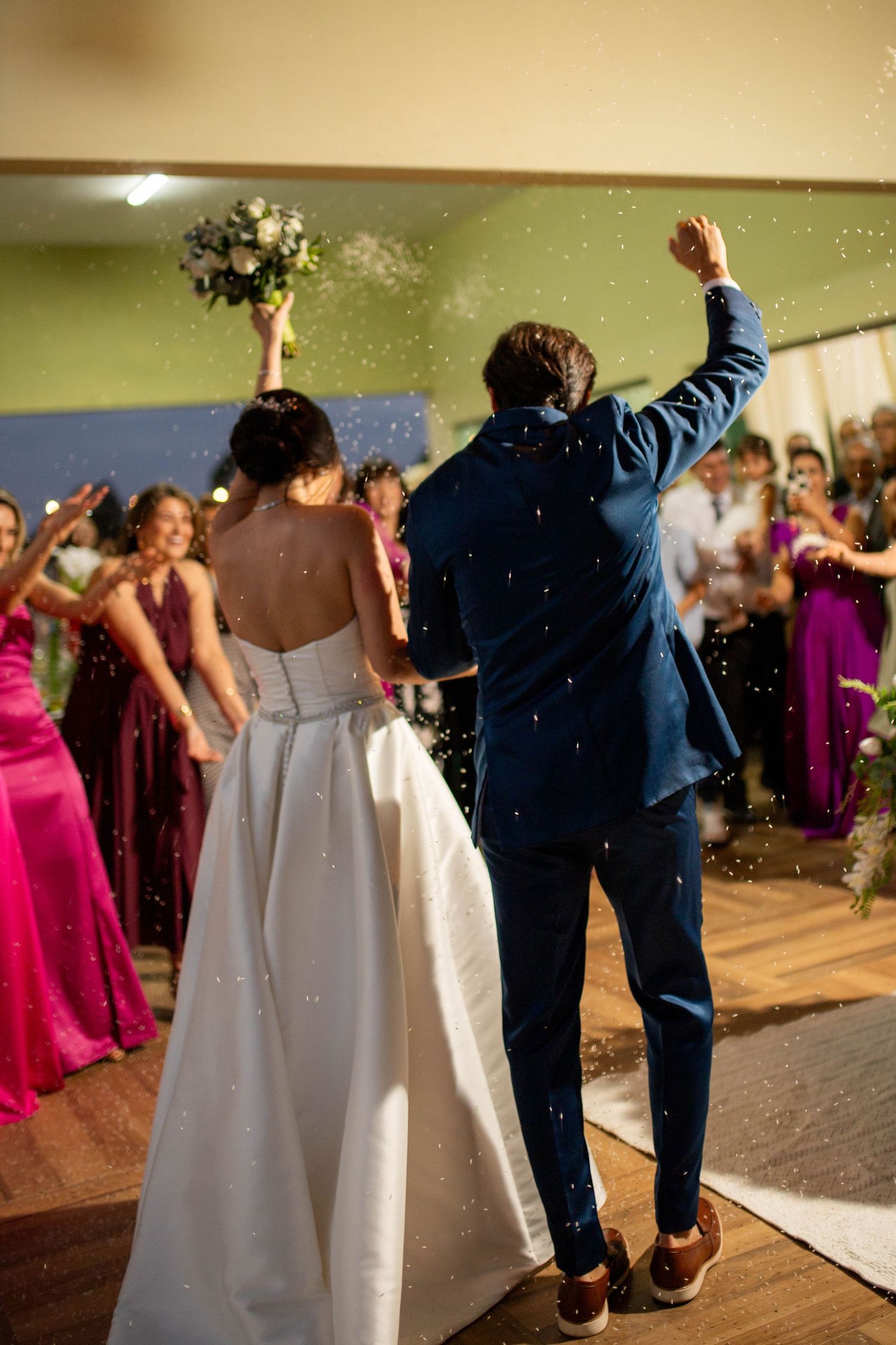 Bride and groom celebrating their first dance with confetti, guests in pink dresses cheering in background.