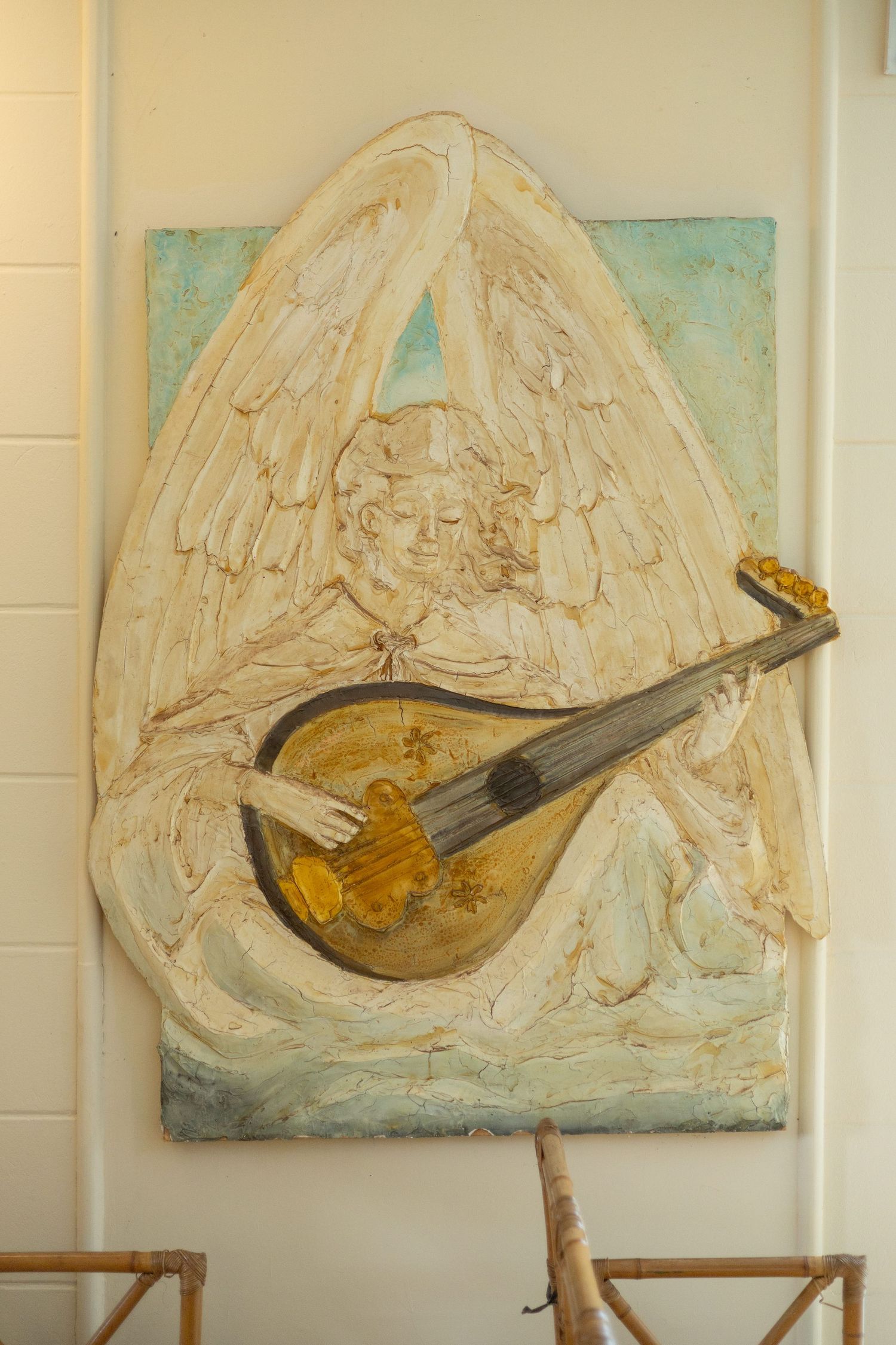 Painting of an angel playing a golden lute, rendered in relief style with white and gold tones on canvas.