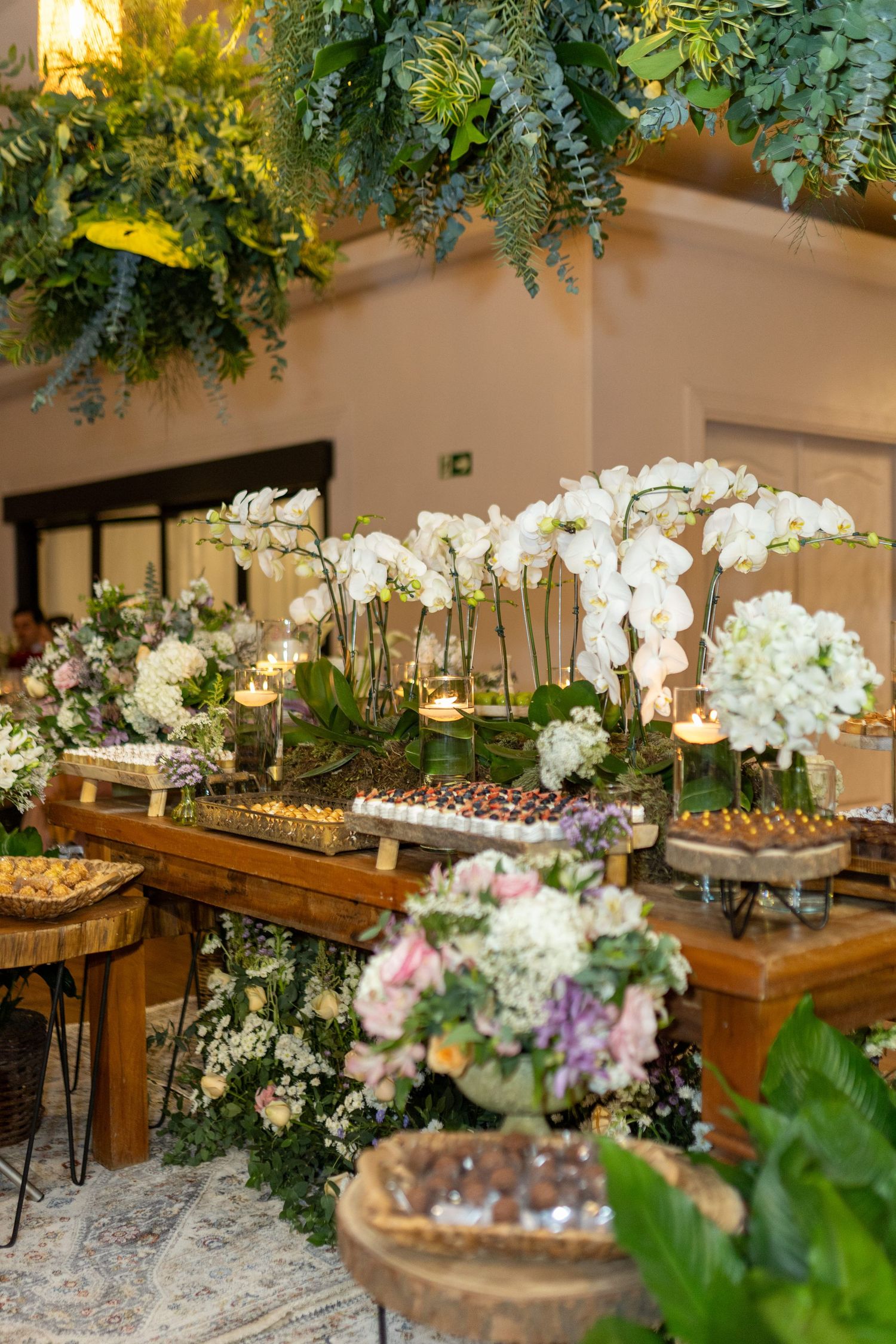 Luxurious wedding dessert table adorned with white orchids, hydrangeas, candles, and assorted sweet treats.