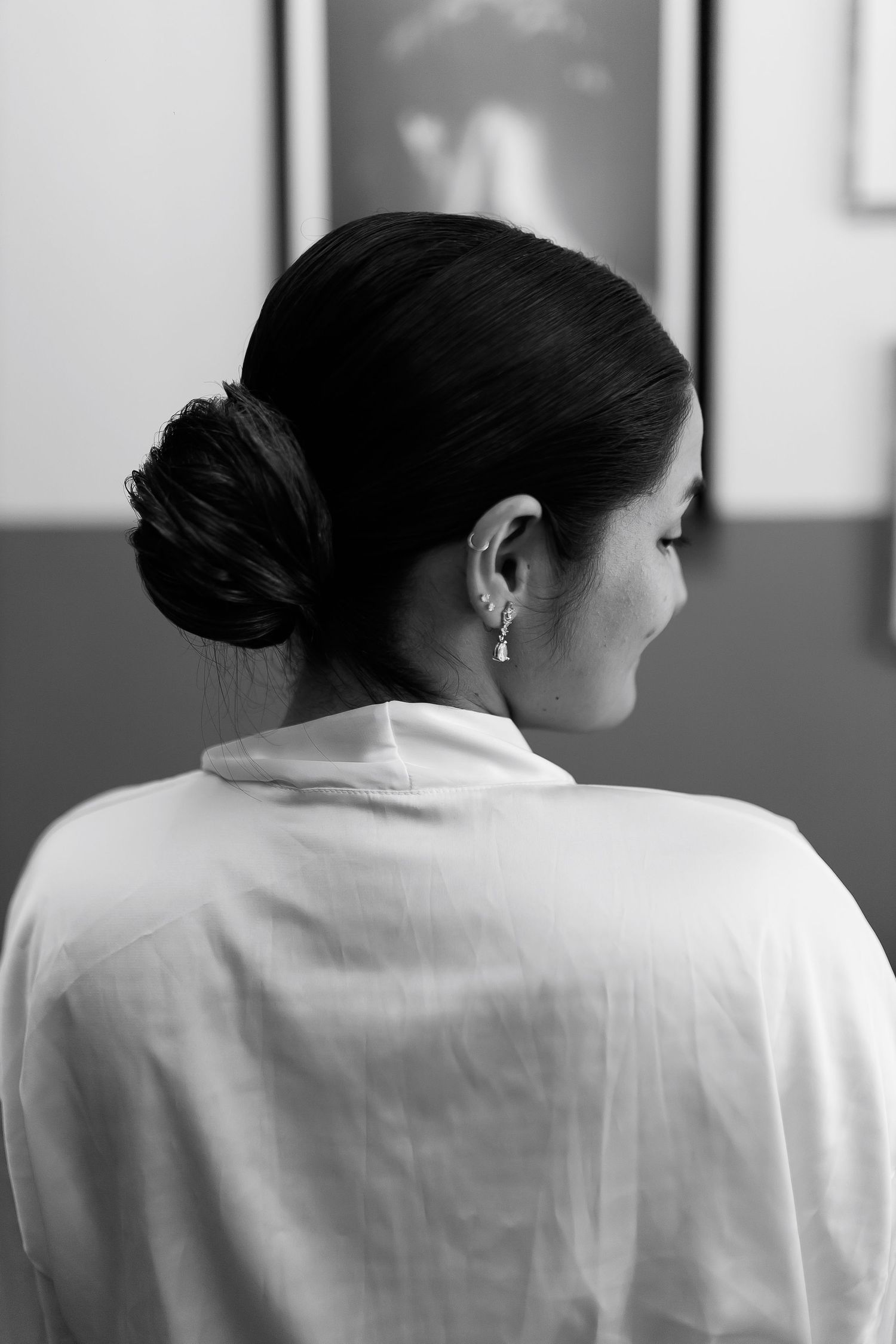Black and white photo of a woman with elegant low bun hairstyle, wearing a white shirt and delicate drop earring.