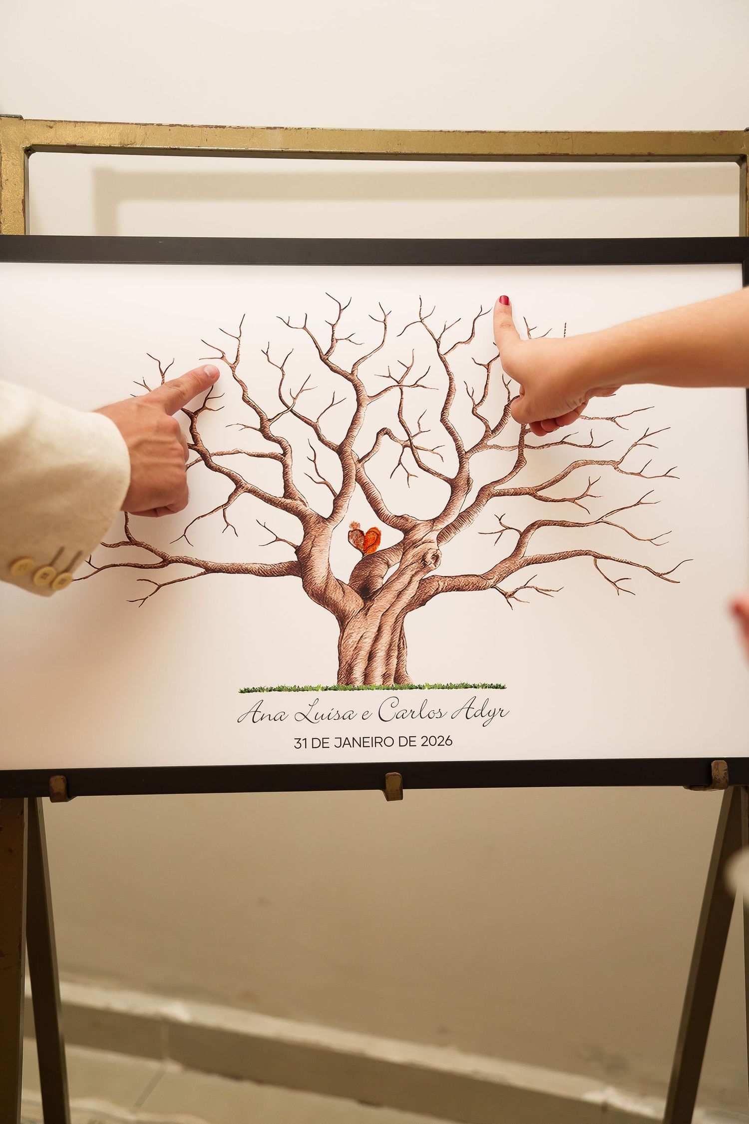 Couple pointing at a wedding fingerprint tree guest book signed Ana Luisa e Carlos Adyr, 31 de Janeiro de 2026.