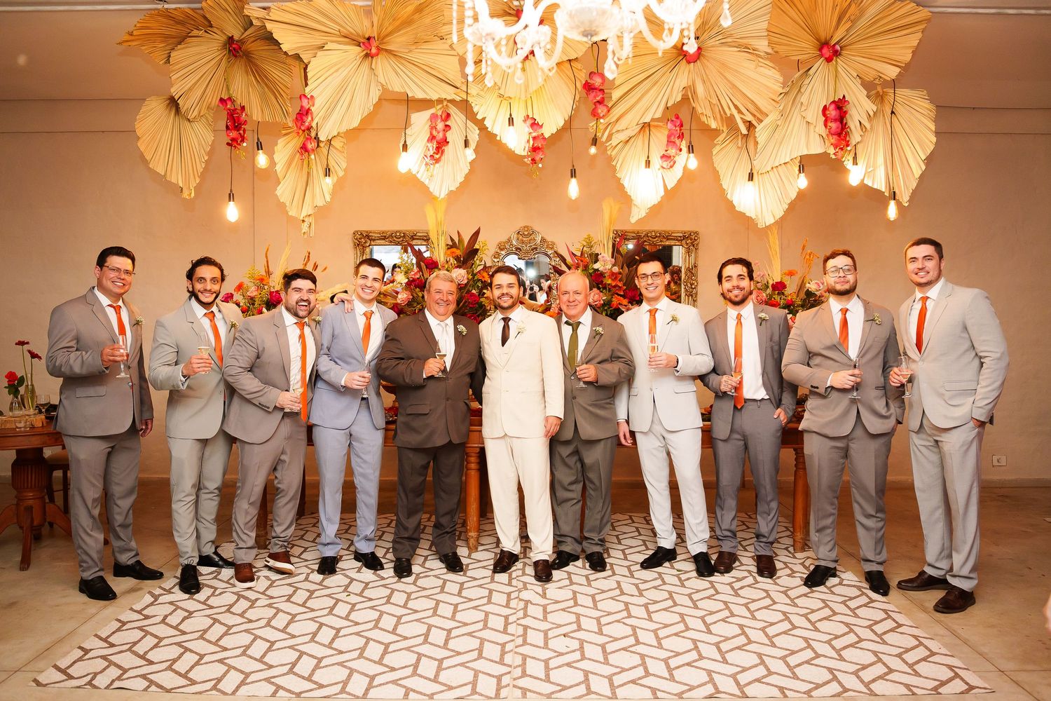 Groom and groomsmen in gray and white suits with orange ties pose together at an elegant wedding venue.