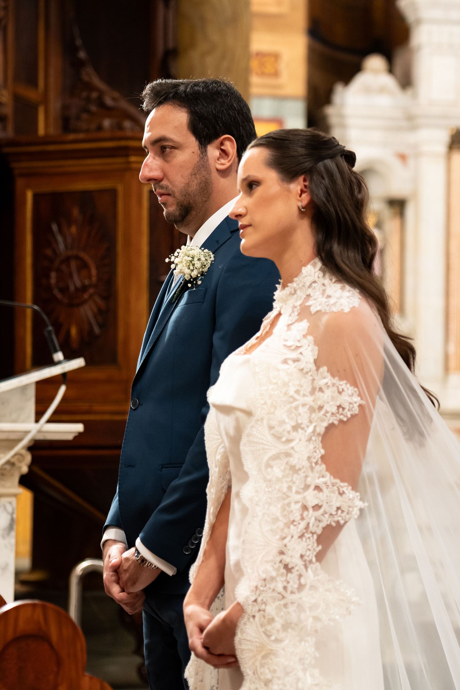 Bride and groom standing together at church altar, bride wearing elegant lace wedding dress with veil.
