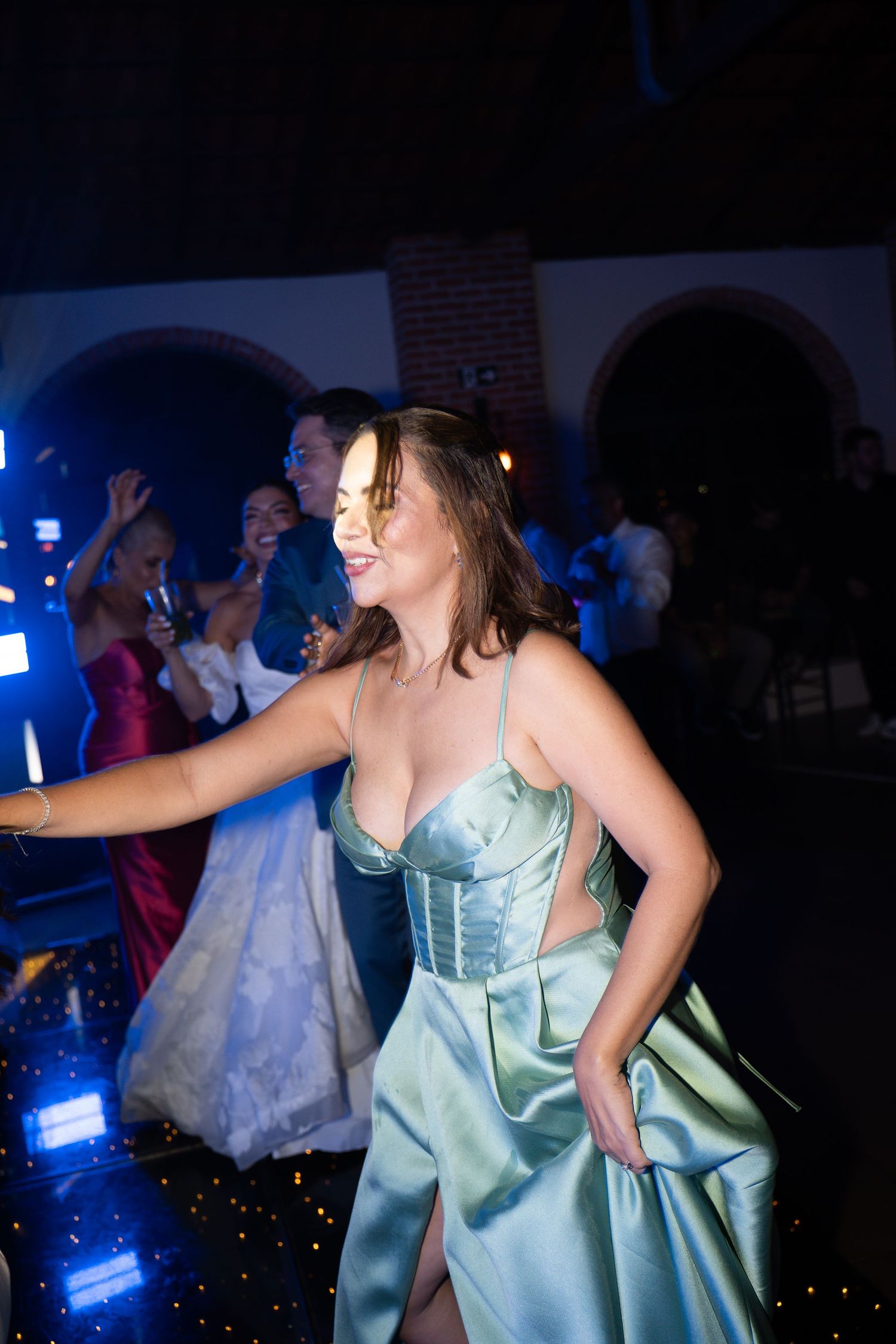 Woman in elegant sage green satin corset gown dancing at a formal event with guests in formal attire in background.