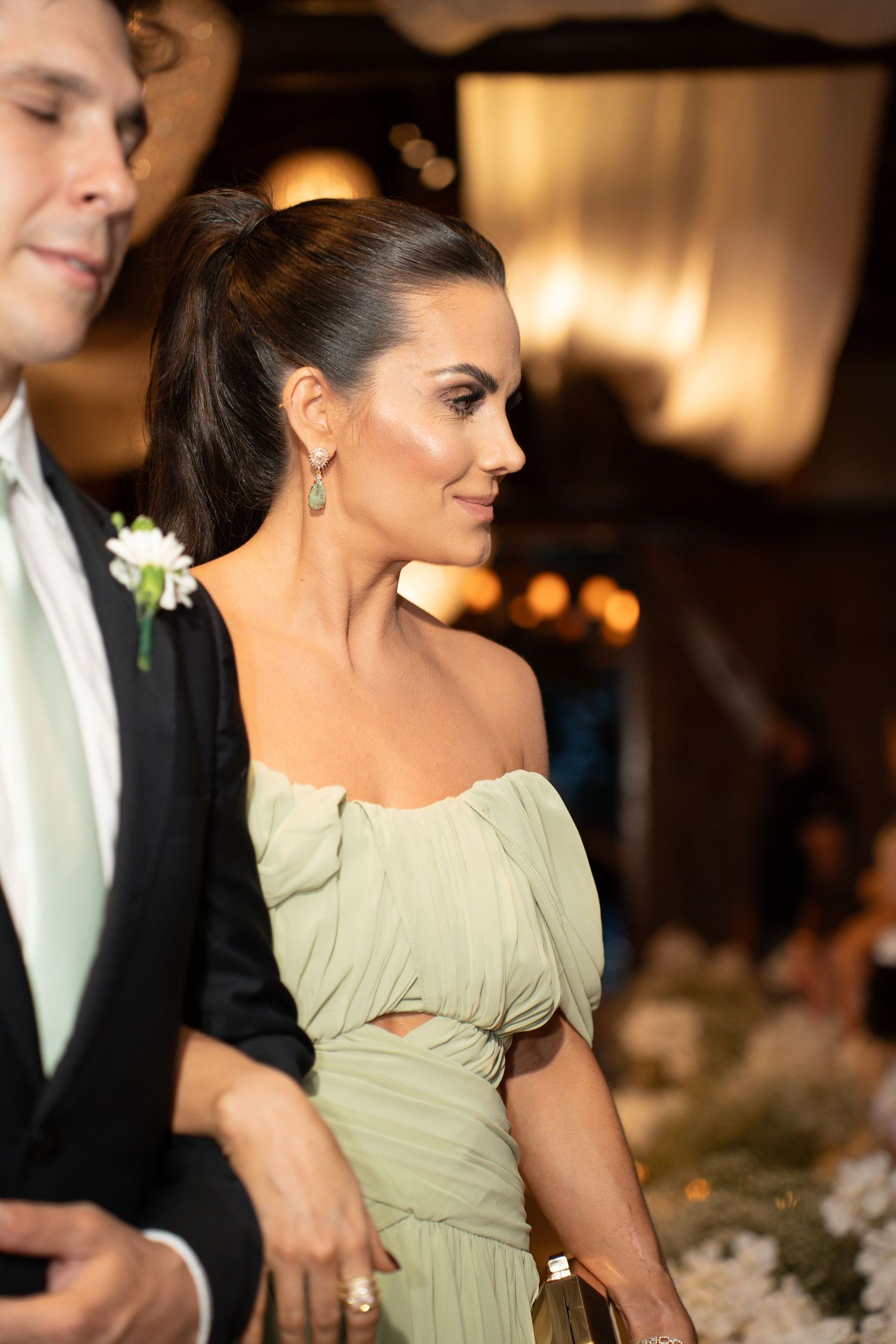 Elegant woman in sage green off-shoulder gown at formal event, wearing drop earrings with hair in updo.