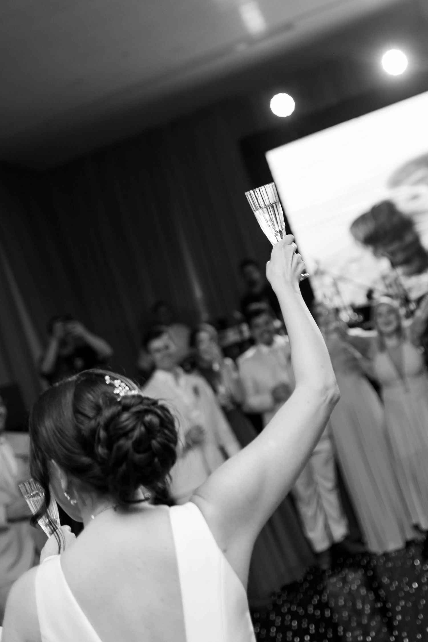 Bride in white dress raises champagne glass at wedding reception in black and white photo.