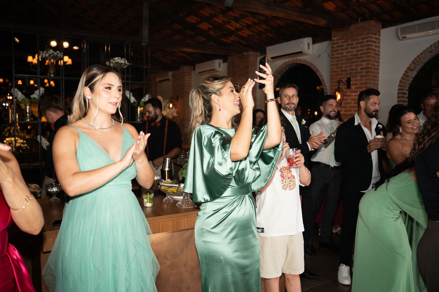 Guests in green dresses dancing and celebrating at an elegant indoor wedding reception party.