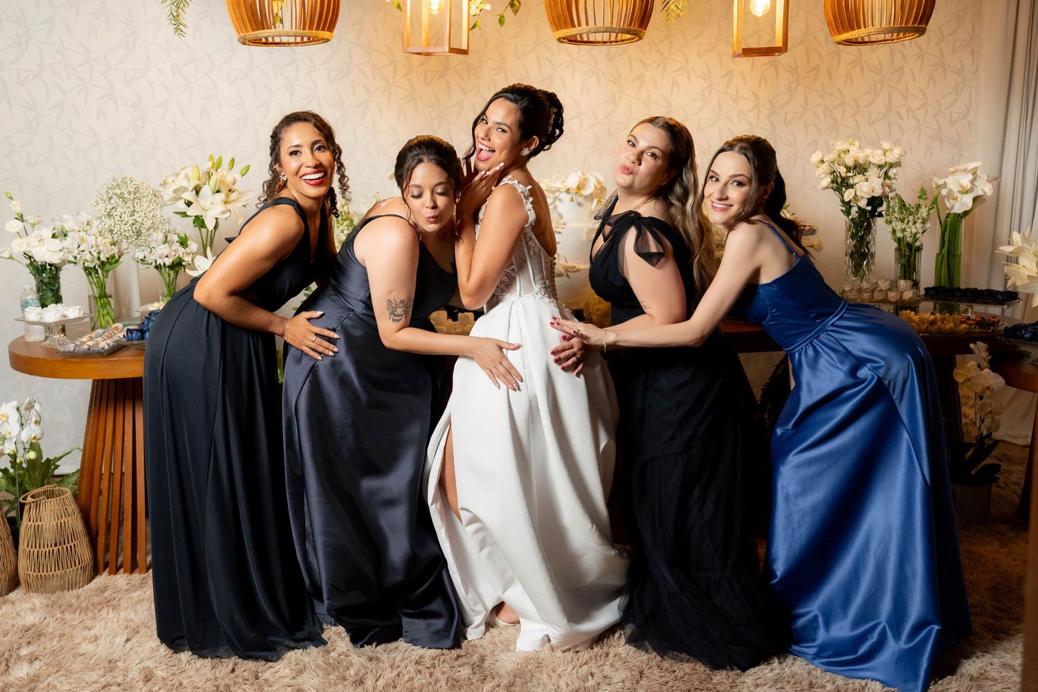 Bride in white gown poses with four bridesmaids in black and blue dresses, smiling together in an elegant venue.